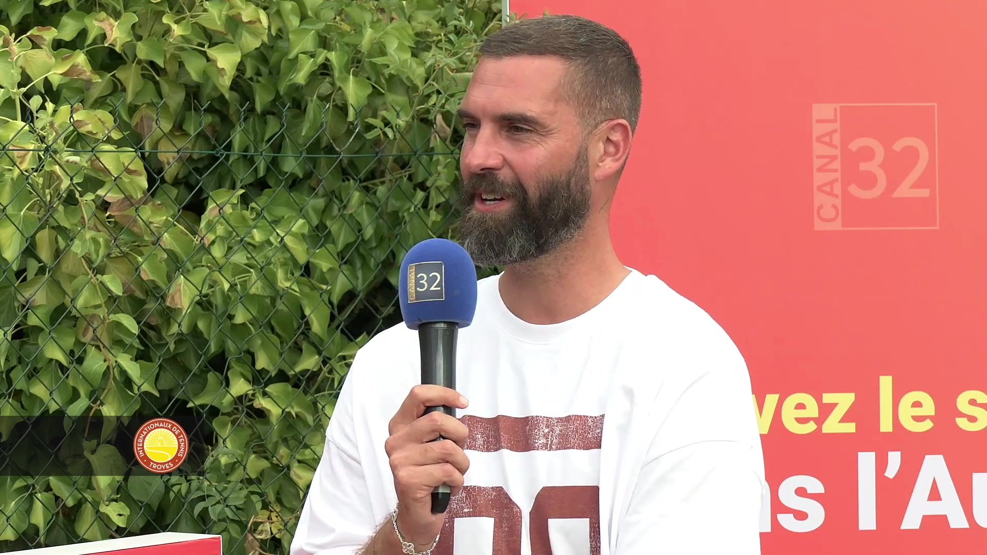 Benoît Paire tient un micro Canal 32 devant un panneau rouge lors des Internationaux de Troyes