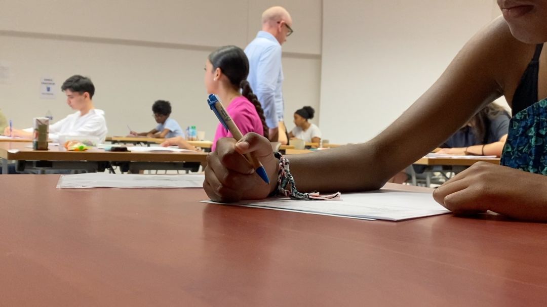 Collégiens rassemblés devant l'entrée vitrée d'un établissement scolaire par ciel bleu dégagé