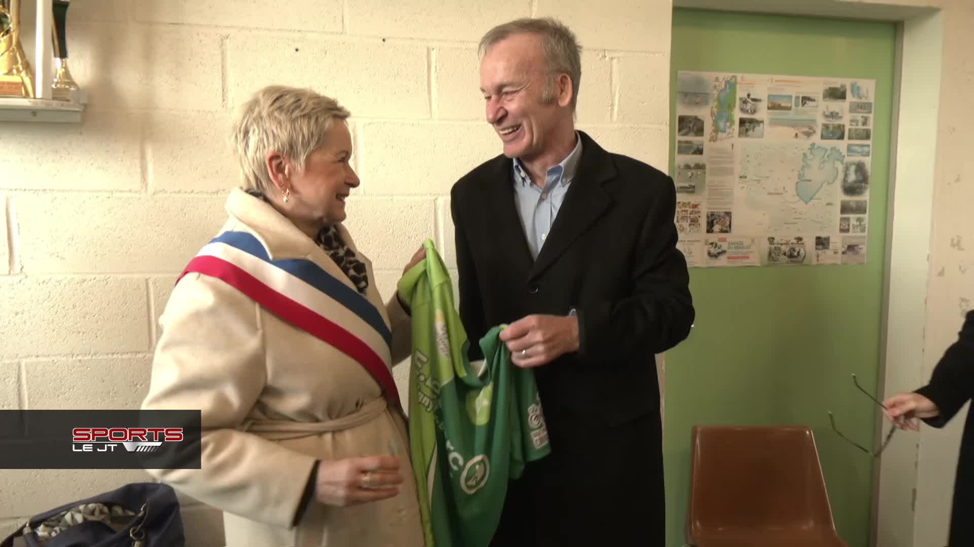 Deux personnes en discussion dans un intérieur, l'une portant une écharpe tricolore, tenant un drapeau vert.