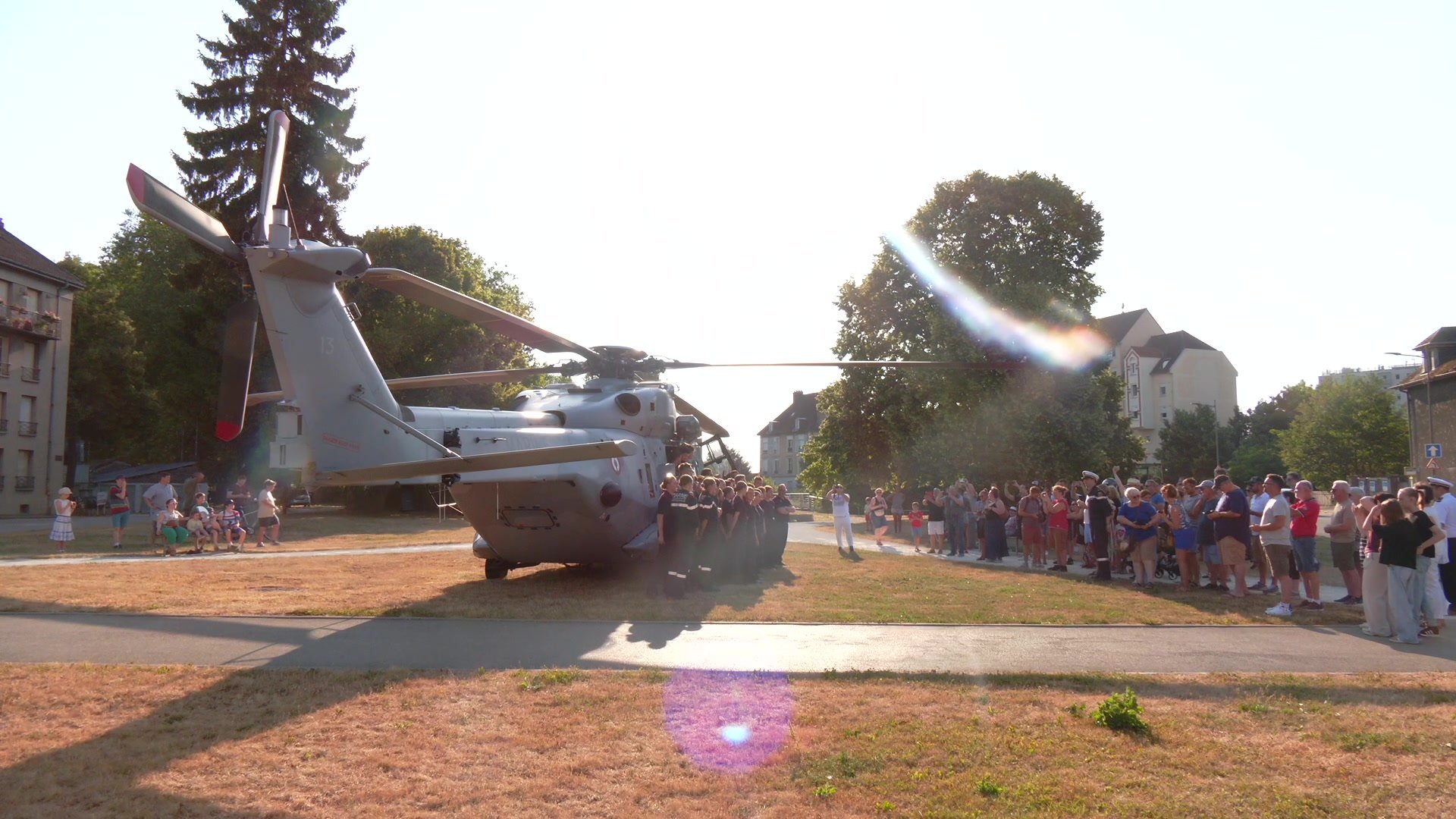 Hélicoptère militaire Caïman posé sur une avenue de Troyes, entouré de badauds, dans un léger voile de poussière au lever du soleil