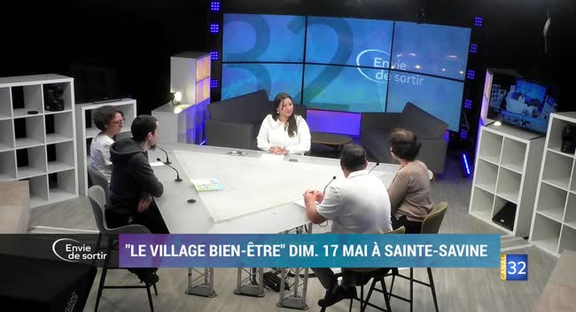 Plateau de tournage avec animatrice et invités autour d'une table, écrans vidéo en arrière-plan