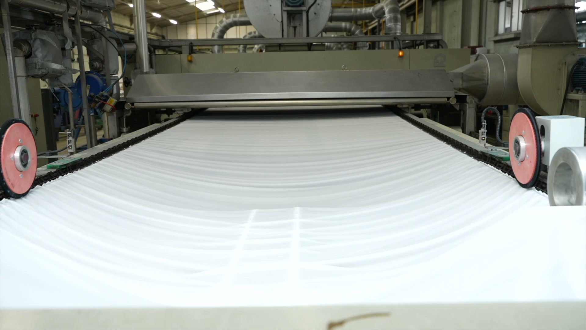 Rouleau de tissu blanc défilant sur une machine industrielle dans un atelier textile