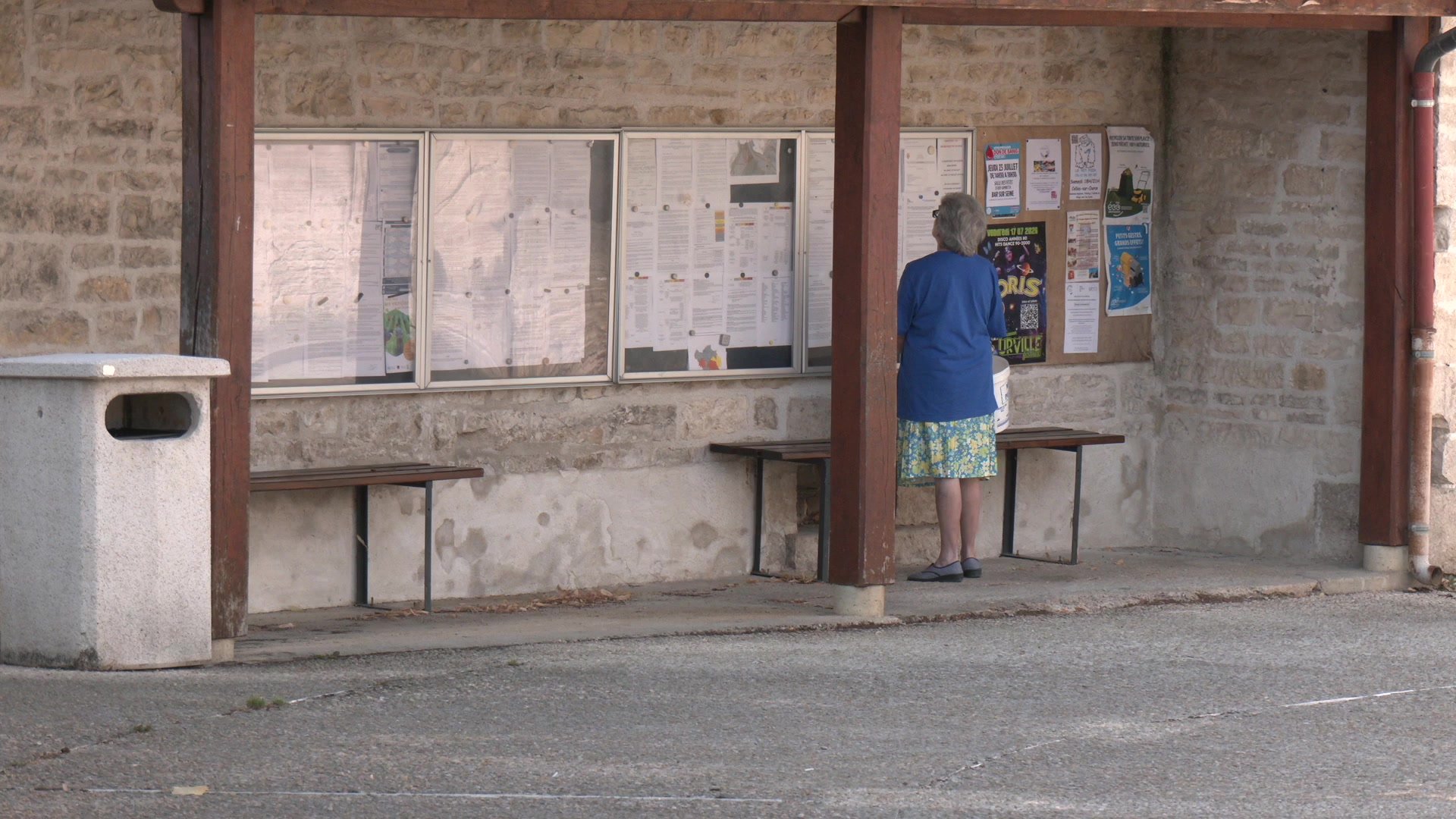 Abri de bus en pierre avec deux bancs et panneaux d'affichage municipaux dans un village