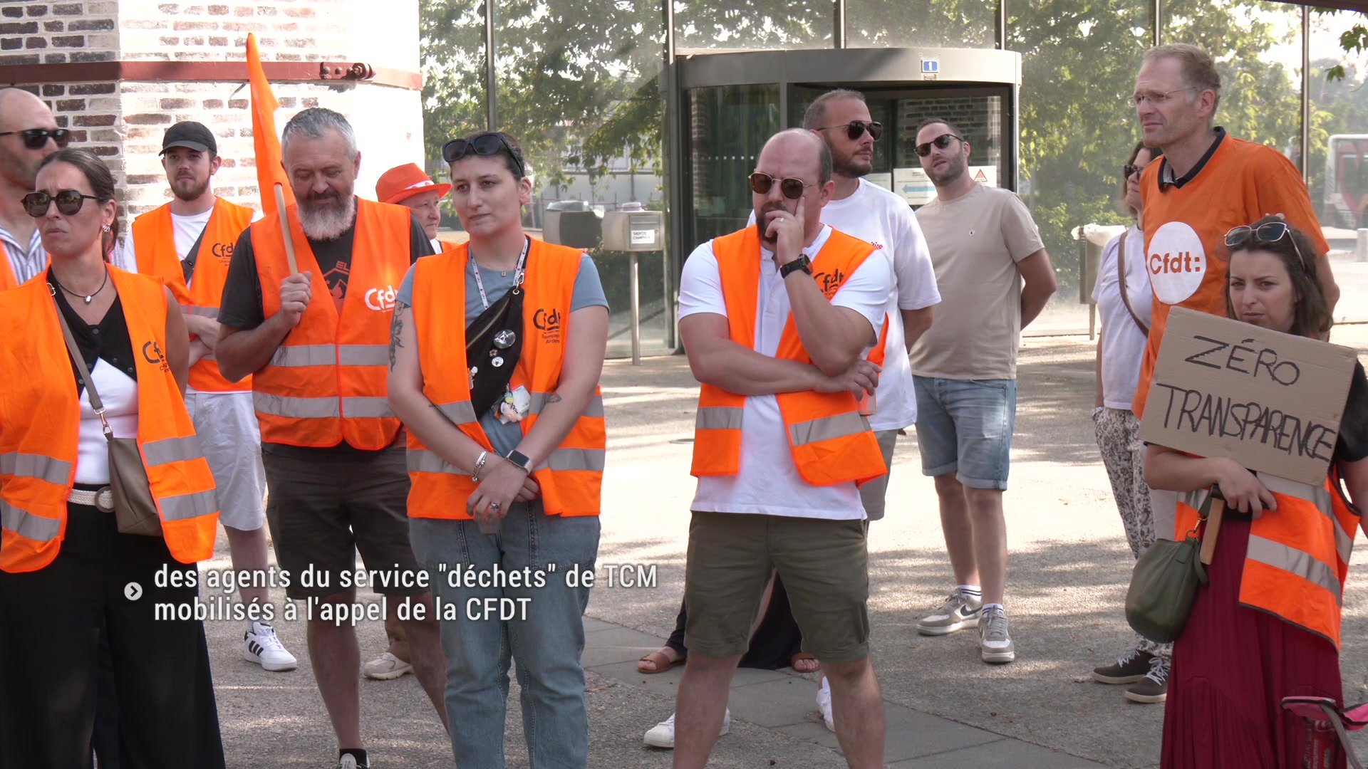 Agents en gilets orange manifestant devant TCM avec pancartes 'Zéro transparence' et 'J'ai mal à mon équité'