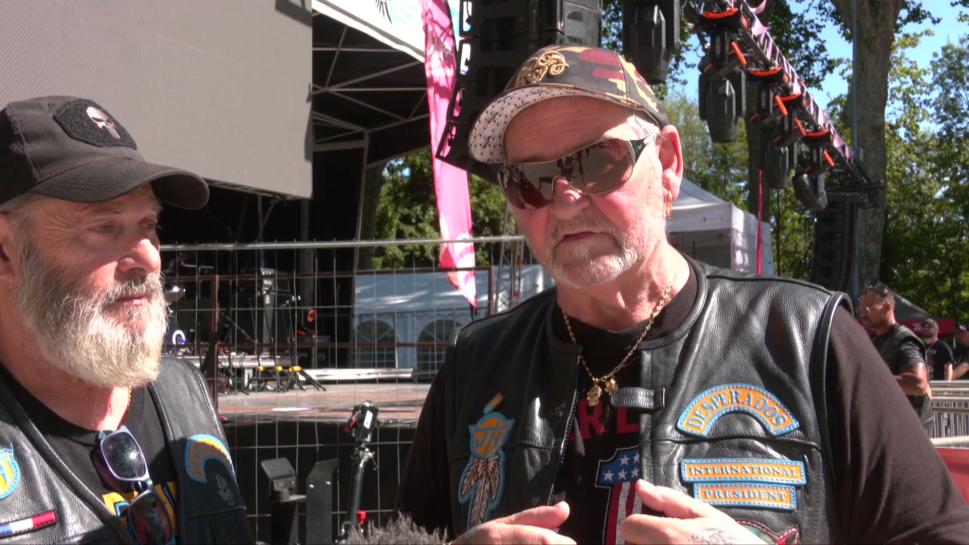 Deux membres des Desperados en veste de cuir avec patches devant une scène de festival en plein air