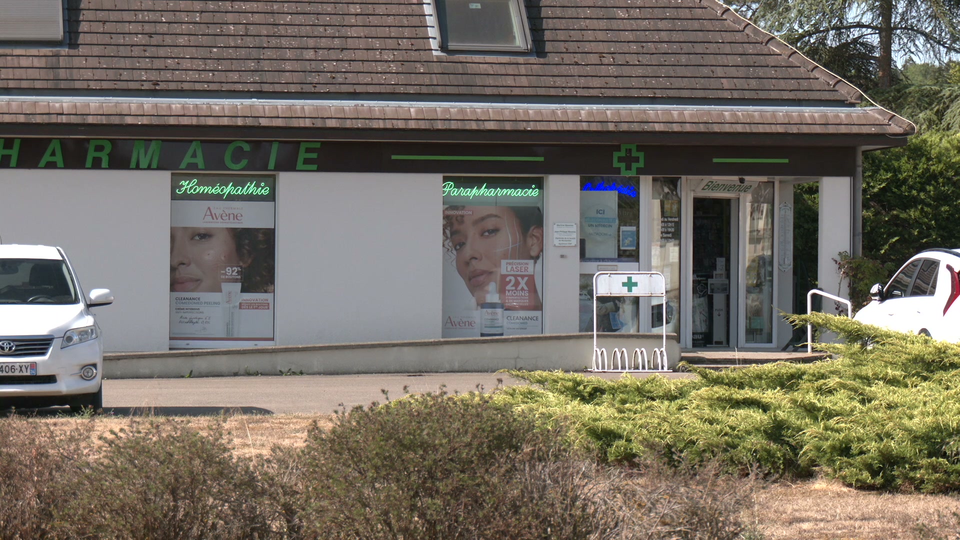 Façade d'une pharmacie avec croix verte lumineuse et affiches Avène en vitrine