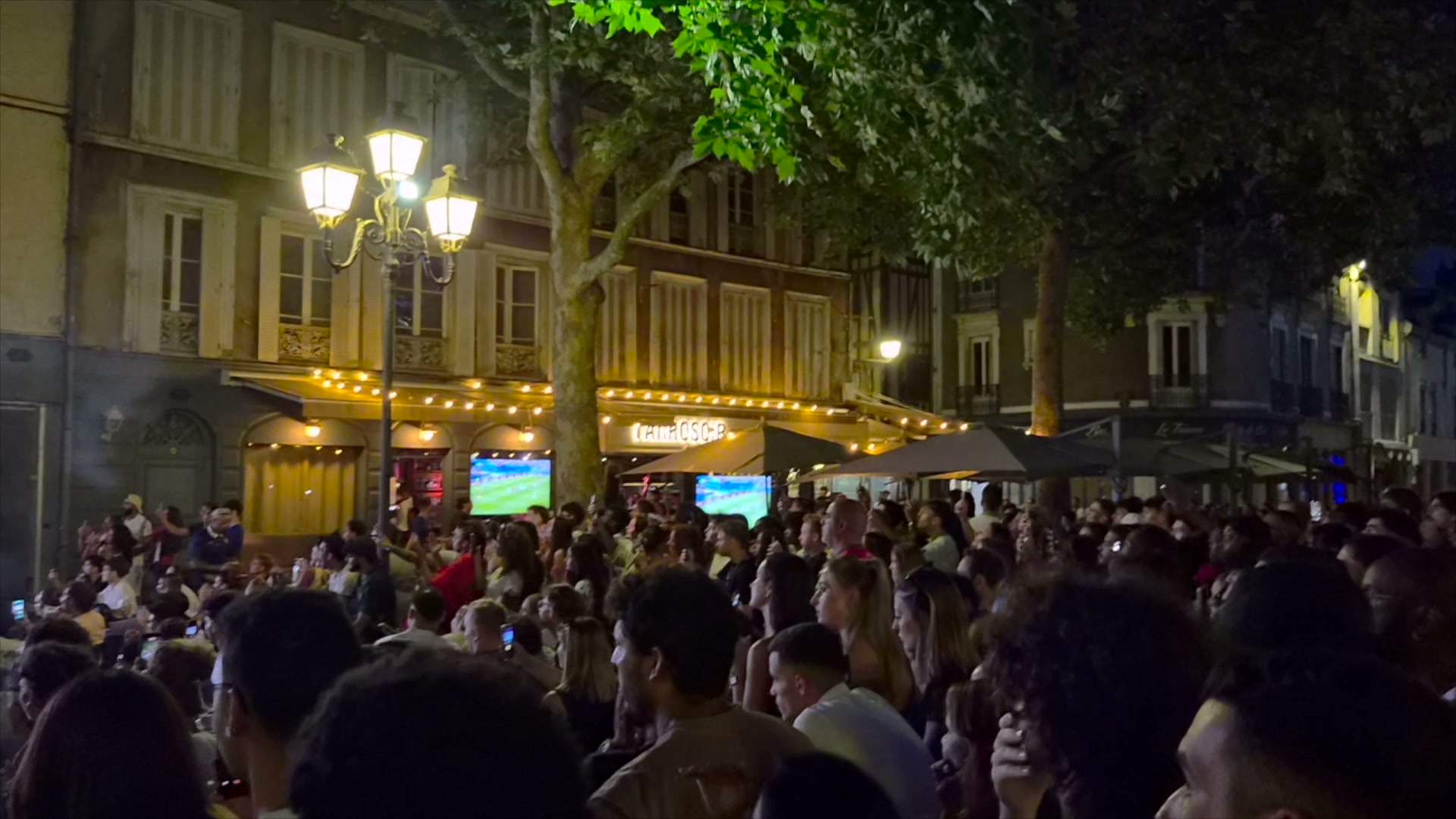 Foule de supporters massée devant un bar aux écrans diffusant un match de football, la nuit, place animée à Troyes