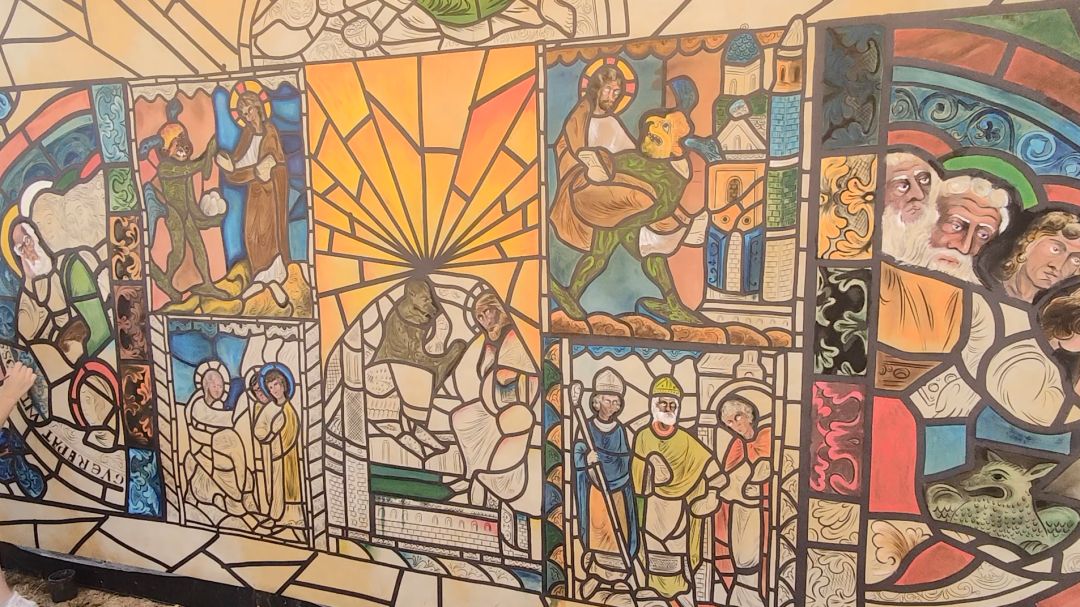 Grande fresque participative imitant un vitrail médiéval avec personnages religieux et scènes bibliques colorées.