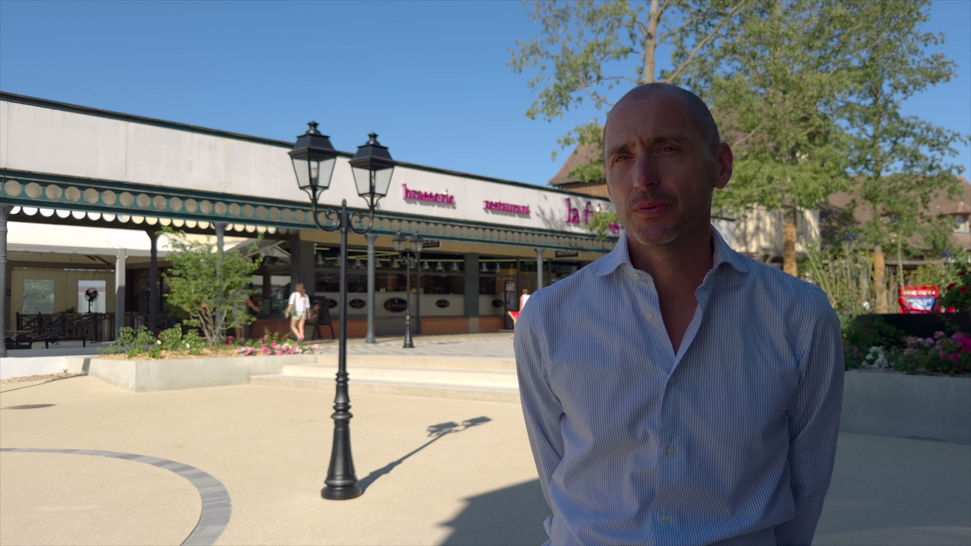 Responsable en chemise rayée interviewé devant la brasserie de McArthurGlen Troyes par temps ensoleillé
