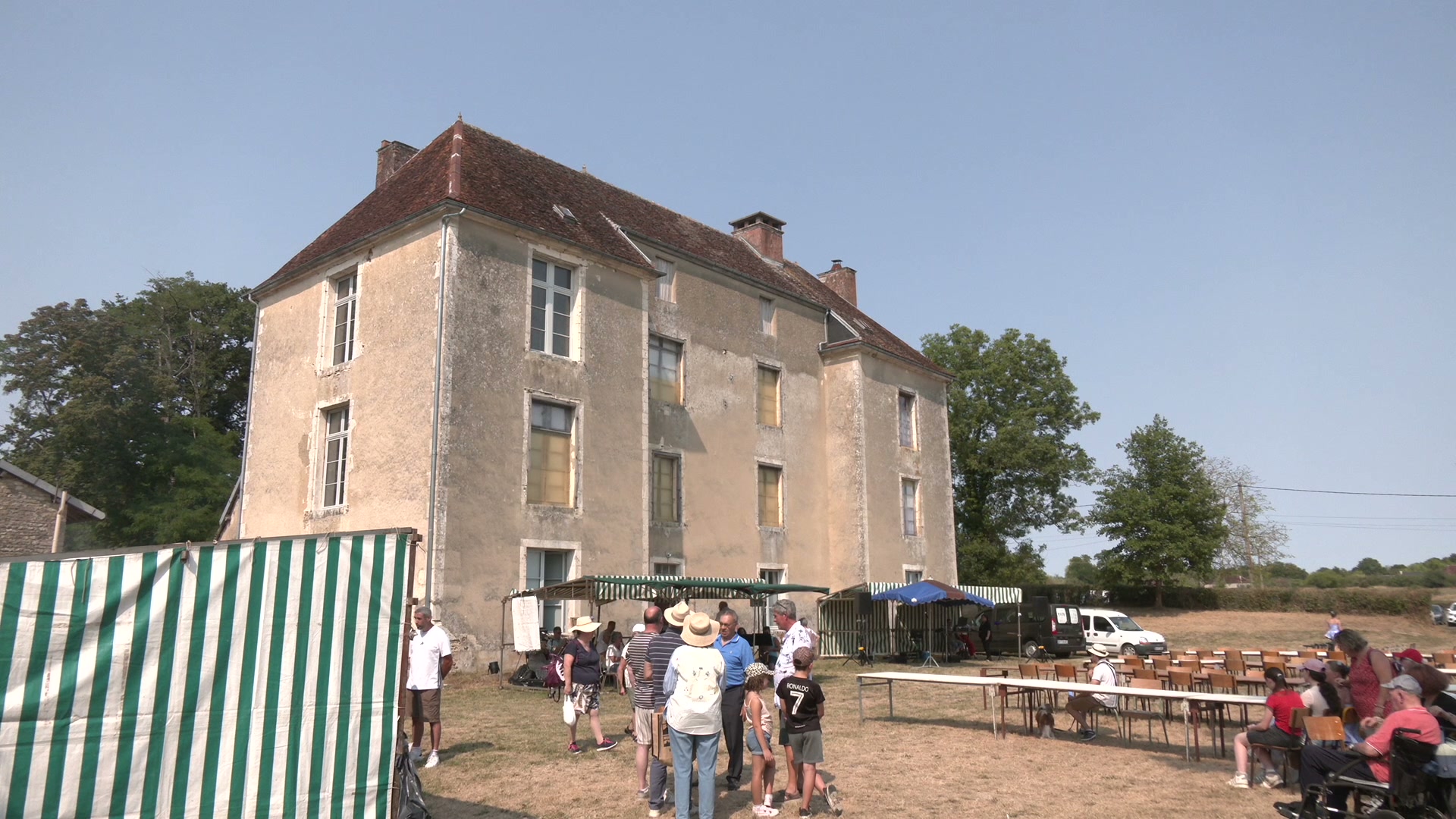 Visiteurs rassemblés devant le château de Turgy sous un ciel bleu, tentes rayées vertes et tables installées dans la cour herbeuse