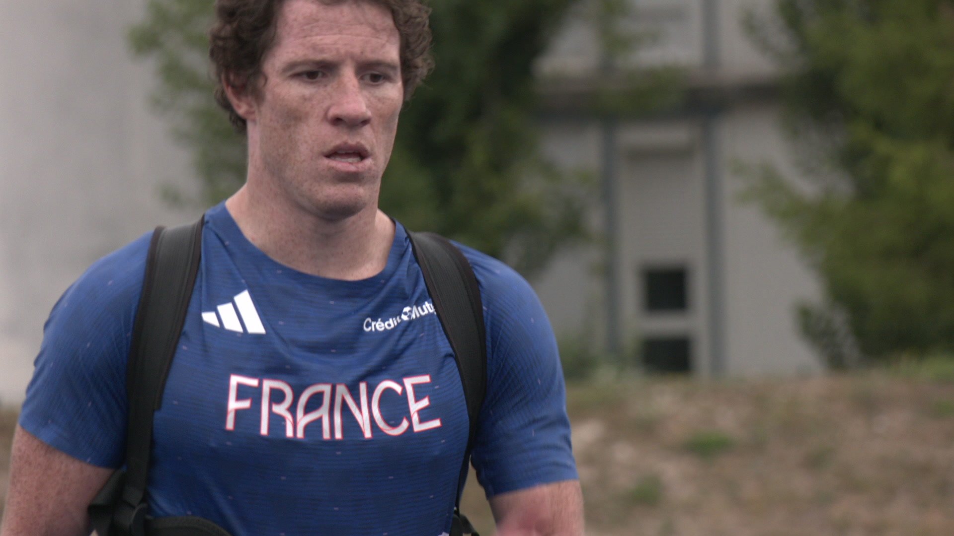 Charles-Emmanuel Roth en maillot France observe un athlète courir sur une piste bleue, sacs et tapis au sol