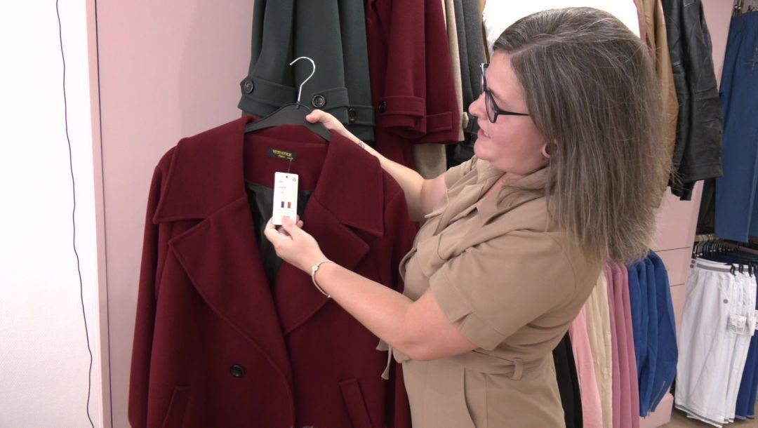 Charlotte Peters présente un manteau bordeaux sur cintre avec étiquette de prix dans sa boutique