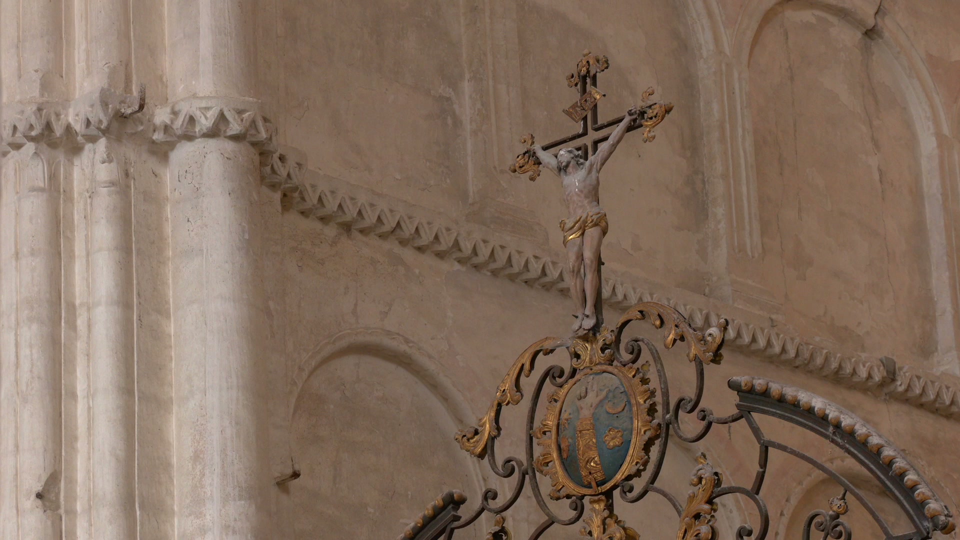 Crucifix doré sur grille en fer forgé ouvragé dans une nef en pierre calcaire