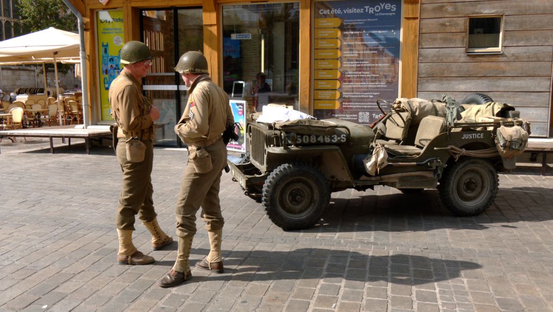 Deux reconstitueurs en uniforme GI conversant devant une Jeep militaire chargée, immatriculée 508463-S, à Troyes