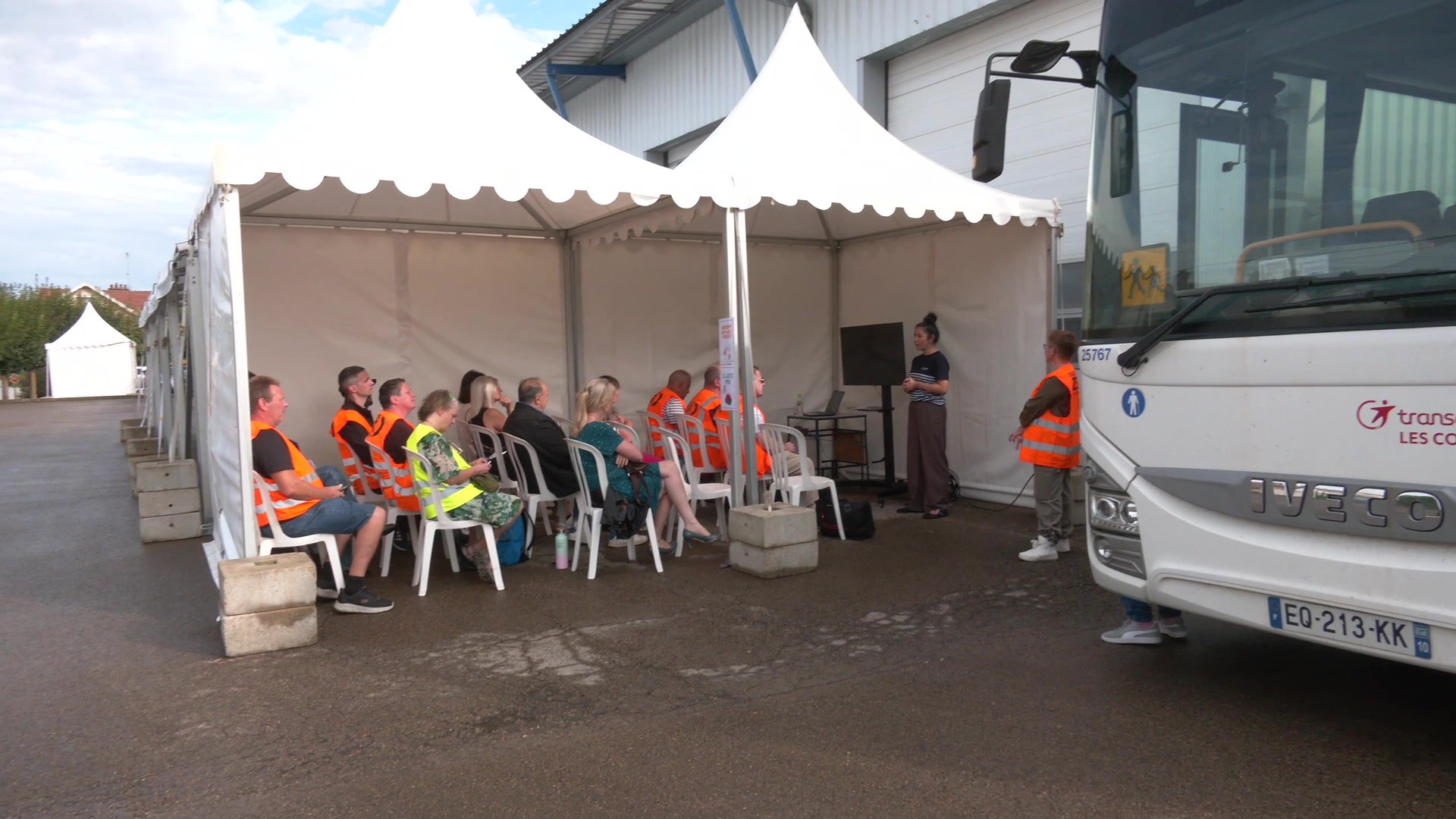 Directrice en gilet jaune fluorescent devant un hangar de maintenance de bus
