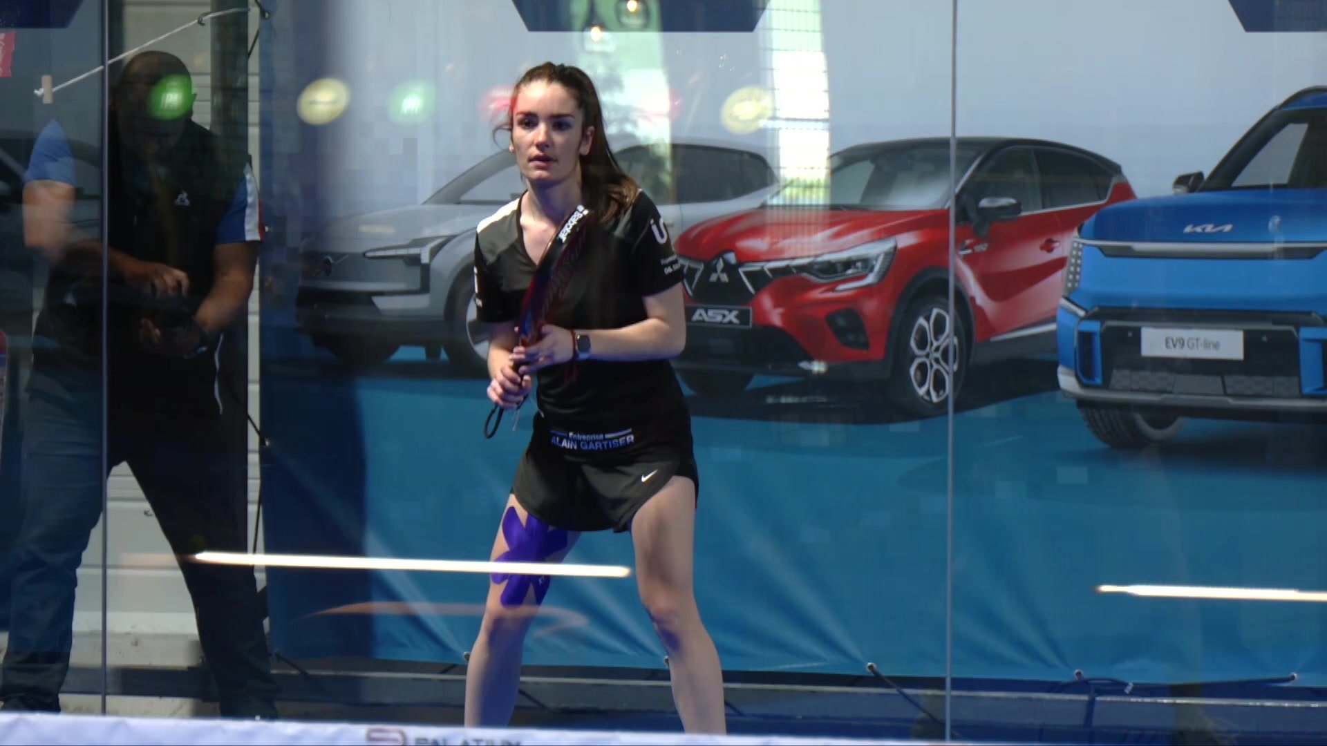 Pauline Robat tenant un micro lors d'une interview dans un club de padel, écran affichant son profil en arrière-plan