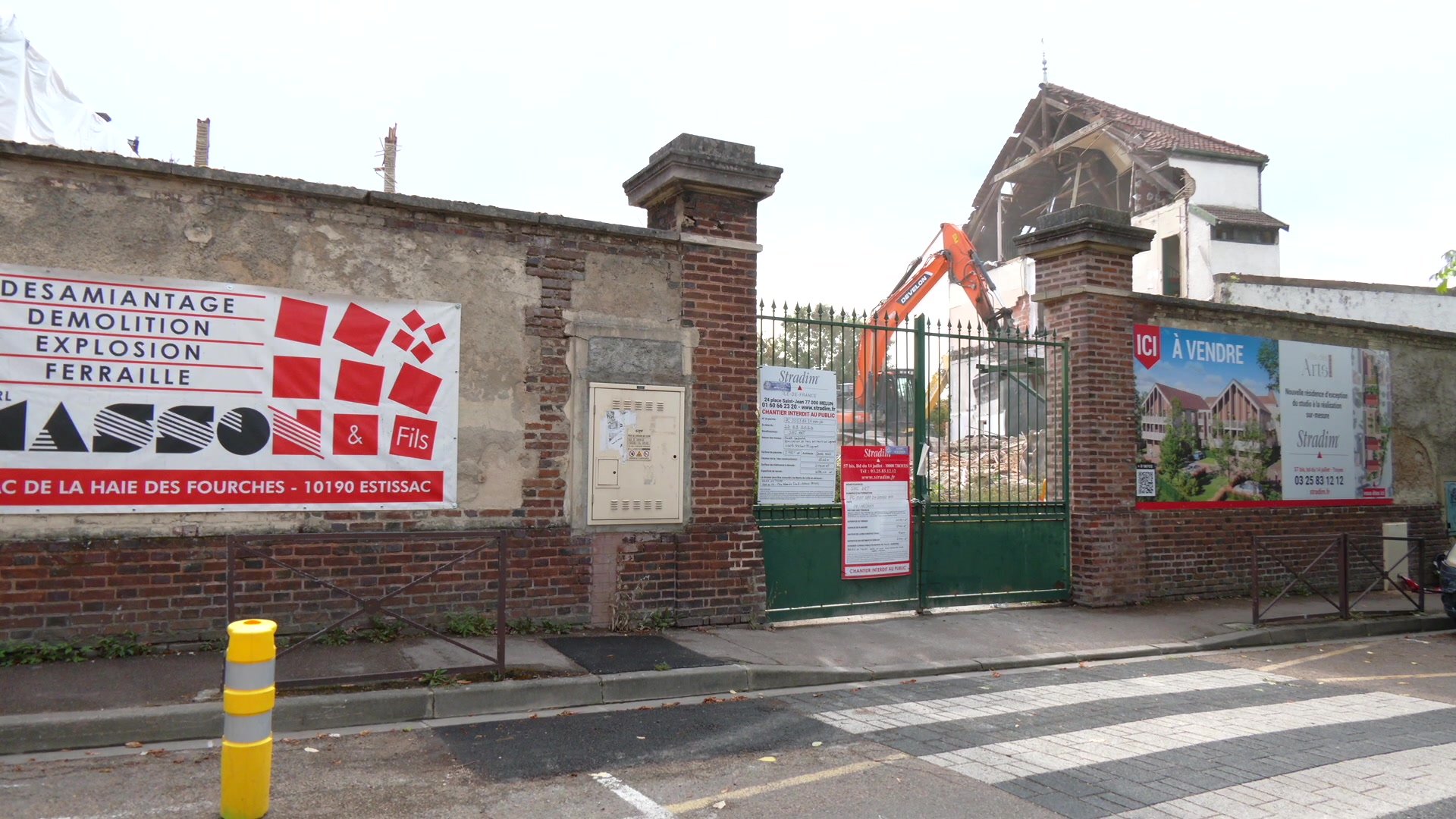 Pelleteuse démolissant les bâtiments de l'ancien collège, murs effondrés et poussière sur le chantier de Troyes