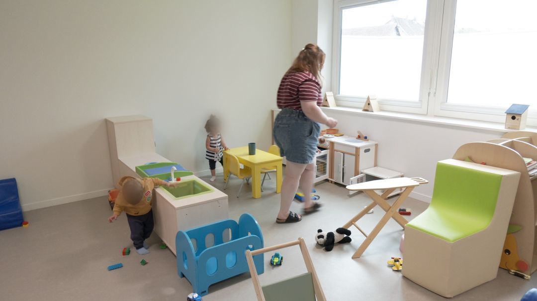 Salle de jeux de la crèche avec jouets colorés, bac de jeu en bois et professionnelle encadrant deux enfants