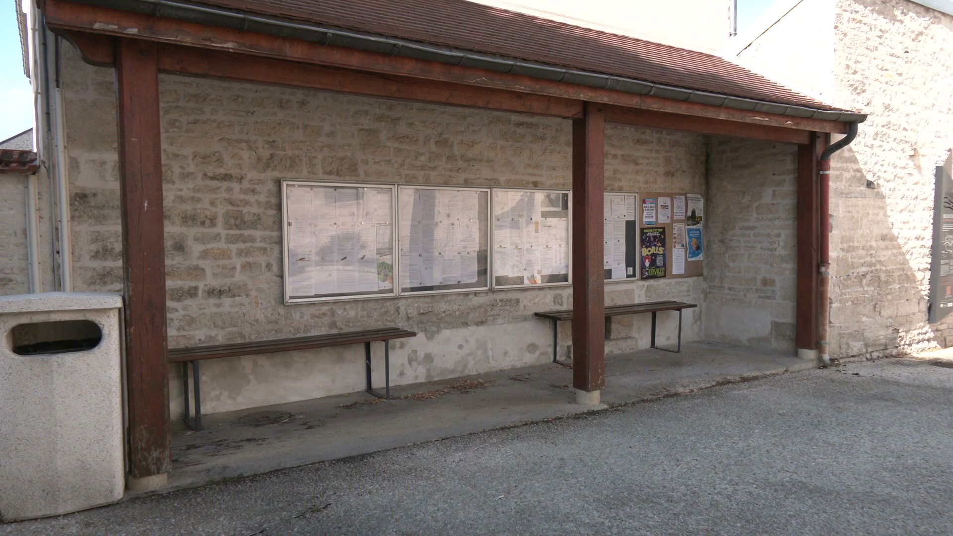 Abri de bus en pierre avec deux bancs et panneaux d'affichage municipaux, village rural de l'Aube