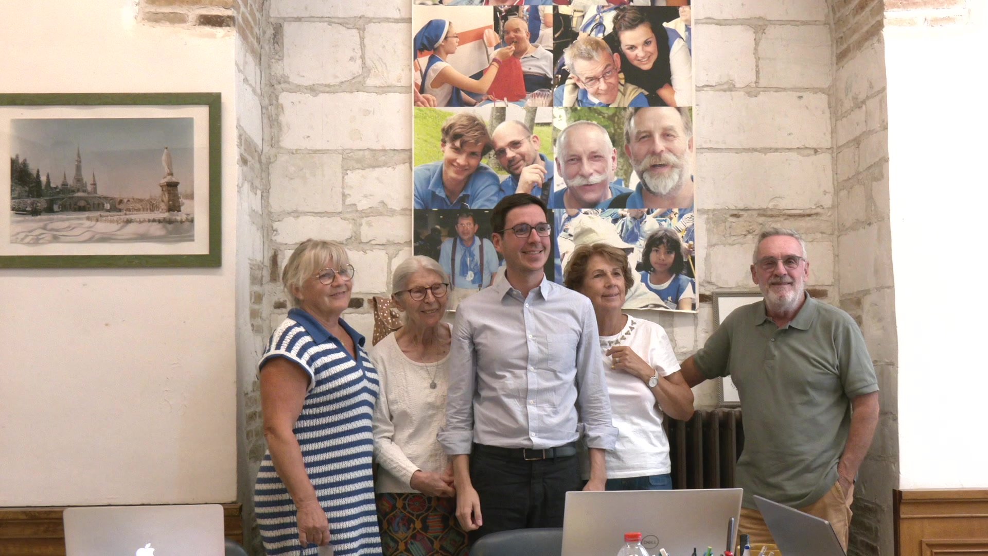 Bénévoles de l'Hospitalité de Champagne autour d'une table avec documents et ordinateur portable, sous un crucifix mural