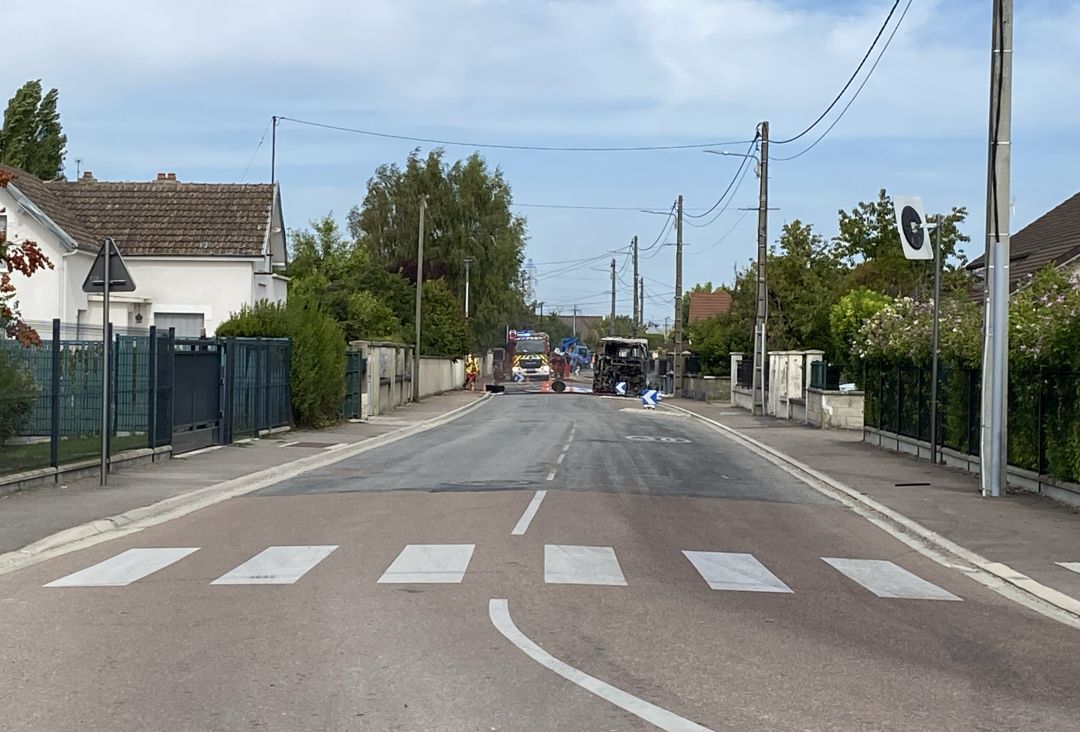 Carcasse calcinée d'un bus immobilisée au milieu de la rue de la Liberté, camion de pompiers visible en arrière-plan