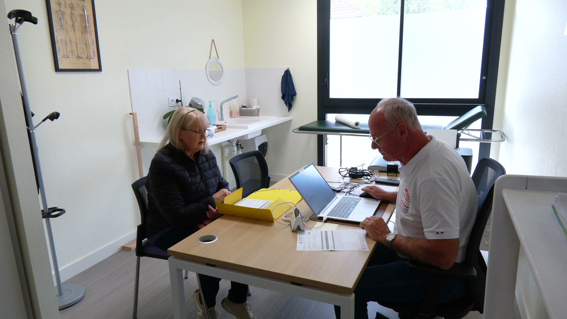 Consultation médicale dans un cabinet, patiente avec chemise jaune face à un médecin devant un ordinateur portable