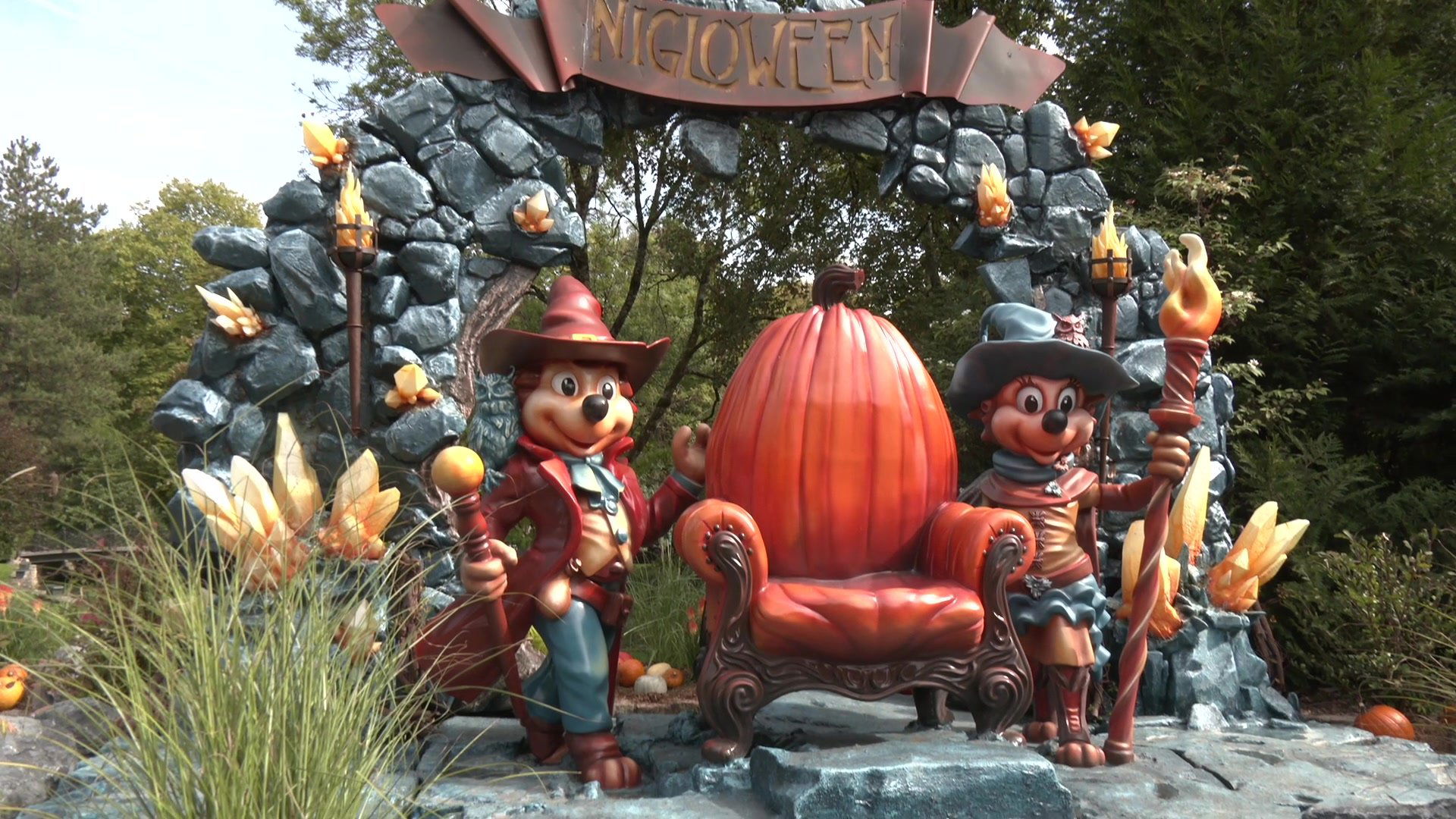 Deux personnages Niglot en costume devant un trône citrouille géant sous une arche en pierre avec l'inscription Niglowee