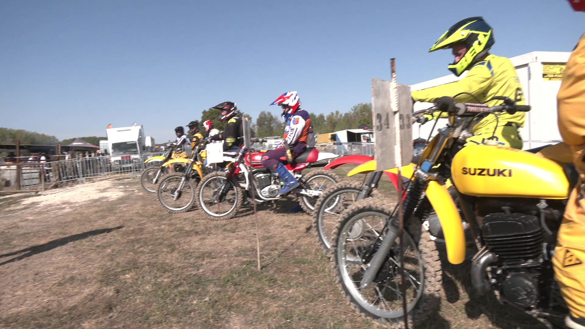 Homme en casquette Fédération Française Moto avec accréditation au cou, parc de véhicules en arrière-plan