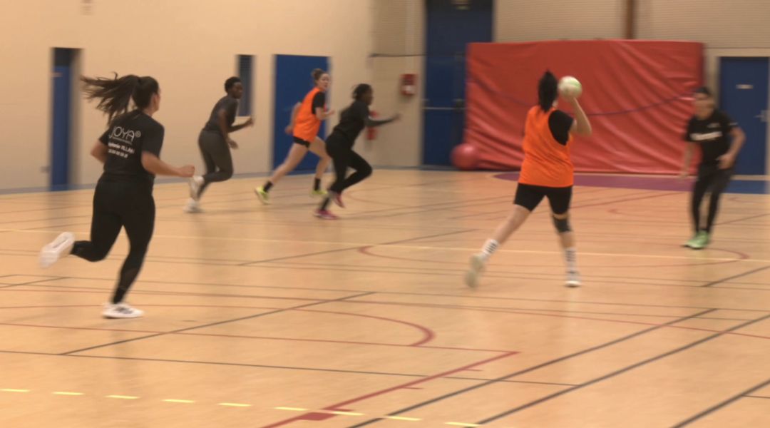 Joueuses en maillots orange et noir disputant un match de handball en salle