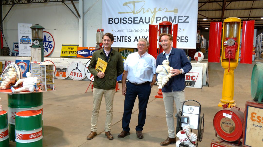 Trois hommes posent devant la bannière Boisseau-Pomez entourés d'automobilia