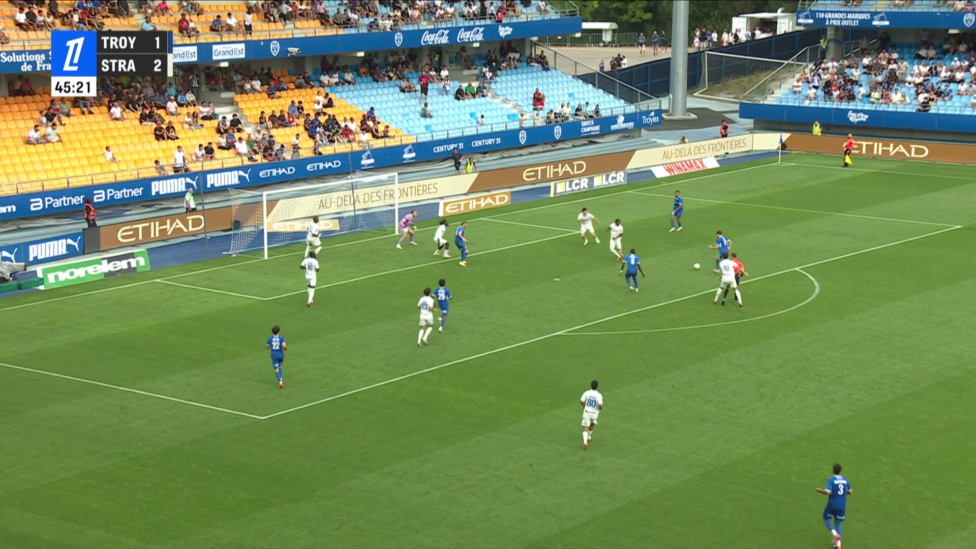 Vue aérienne du Stade de l'Aube, score TROY 1 STRA 2 à la 45e minute, joueurs en maillots bleus et blancs autour de la surface de réparation