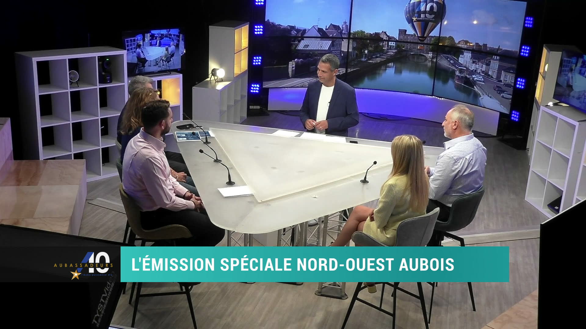 Cinq invités autour d'une table blanche sur le plateau de Canal 32, écran affichant une montgolfière en arrière-plan