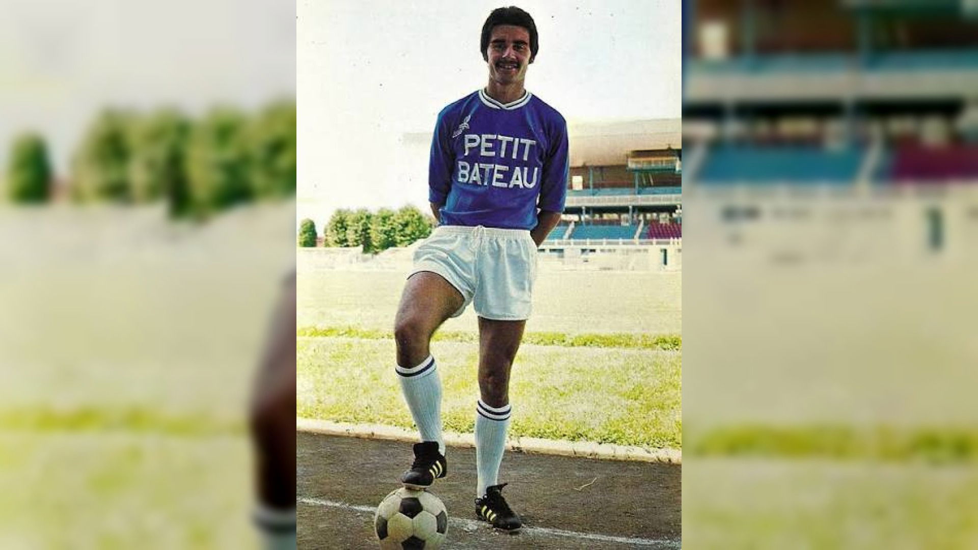 Daniel Zorzetto en maillot bleu Petit Bateau du Troyes Aube Football, pied posé sur un ballon, devant les tribunes du stade