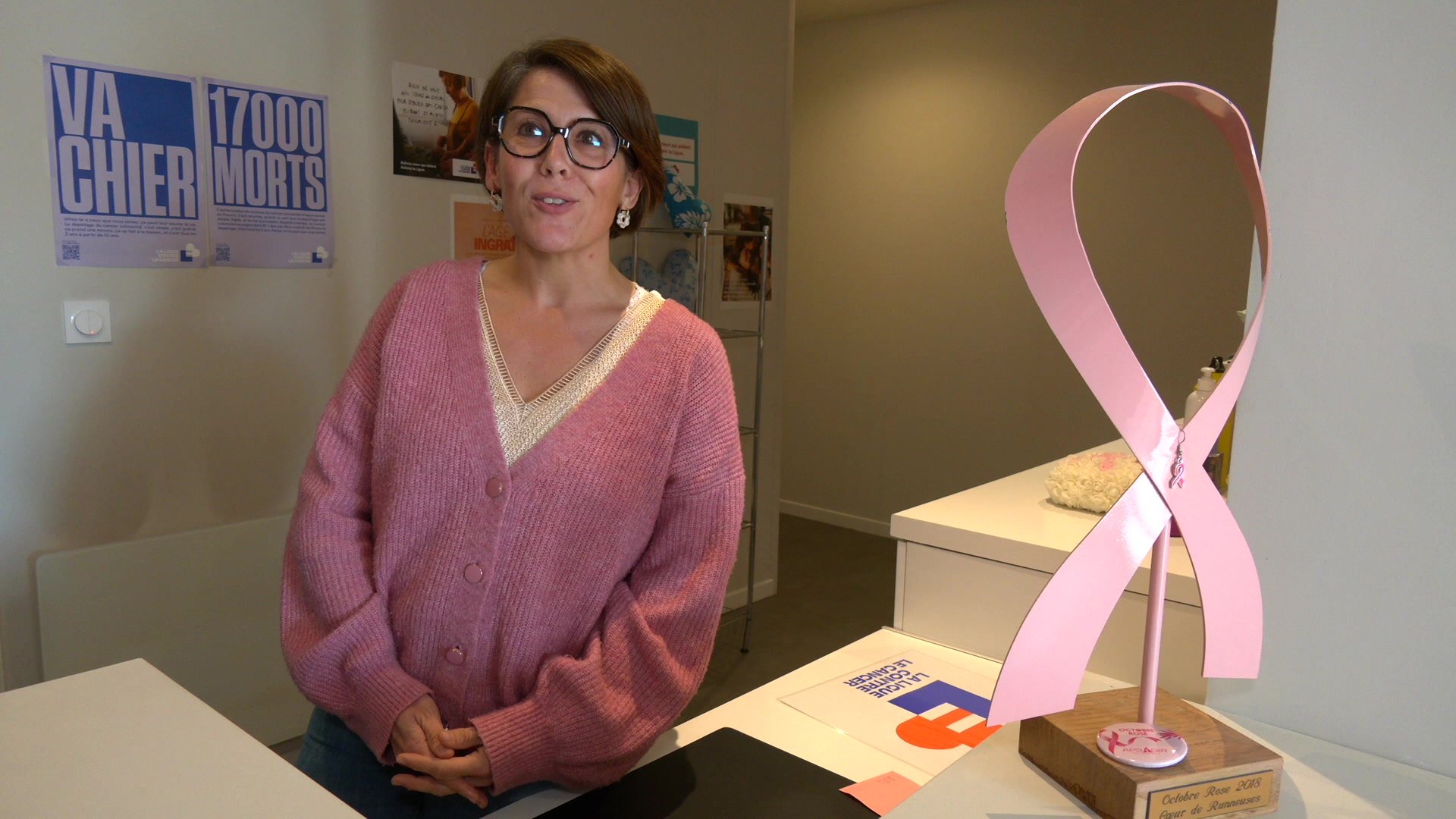 Deux femmes en conversation dans une pièce avec une affiche Octobre Rose accrochée au mur, table en bois et sac doré au premier plan