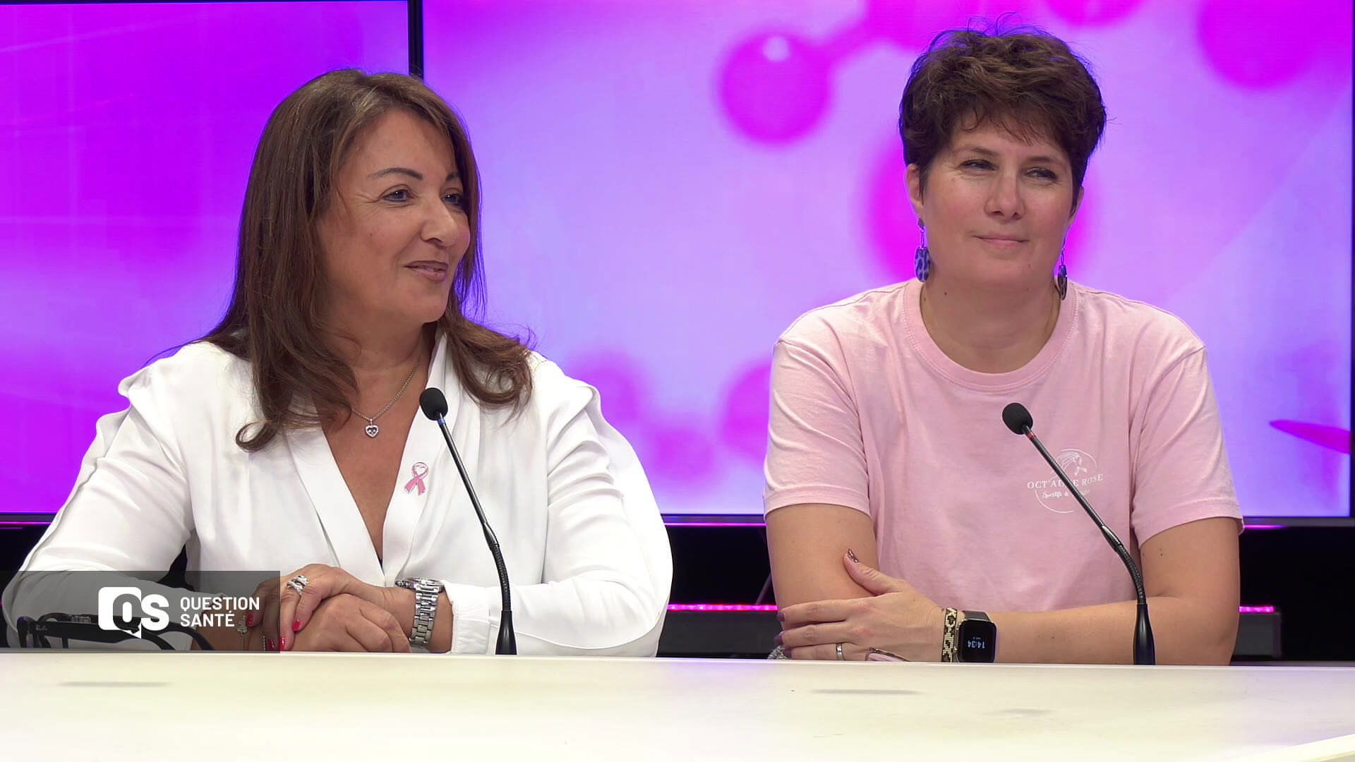 Deux invitées souriantes sur le plateau de Question Santé, fond rose, ruban rose épinglé sur veste blanche