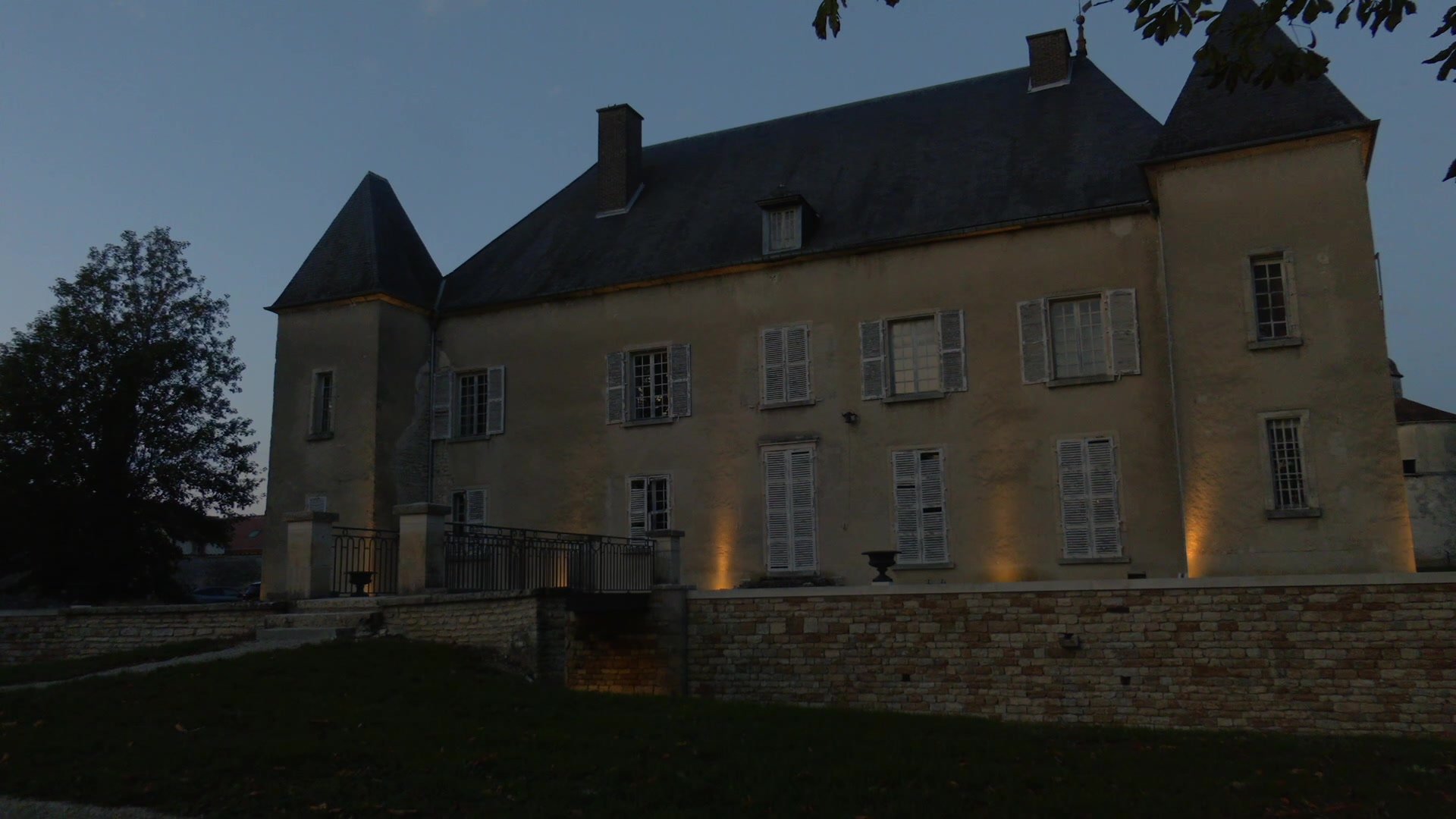 Façade du château d'Ailleville avec ses deux tours à toits ardoisés photographiée au crépuscule, ciel bleu pâle, escalier en pierre au premier plan