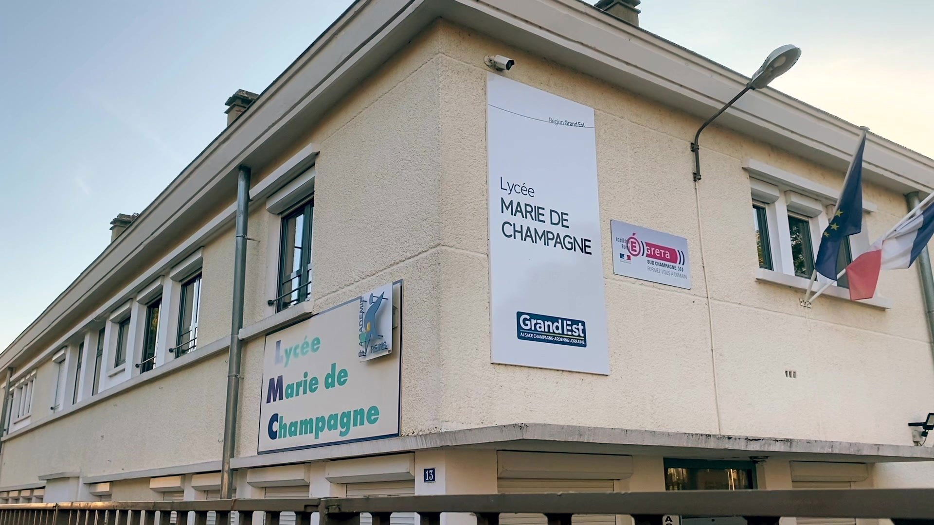 Façade d'un lycée avec drapeaux français et européen, cour déserte et portes vitrées à l'entrée