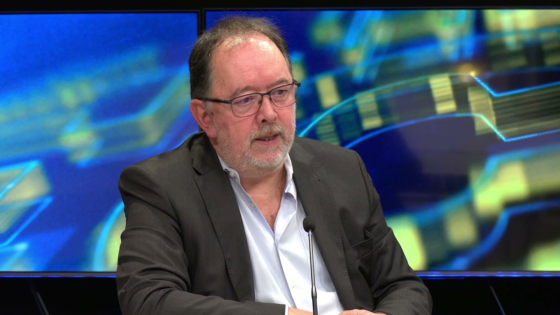 Gilles Burysek, veste grise et chemise blanche, prend la parole devant un micro sur le plateau de Canal 32