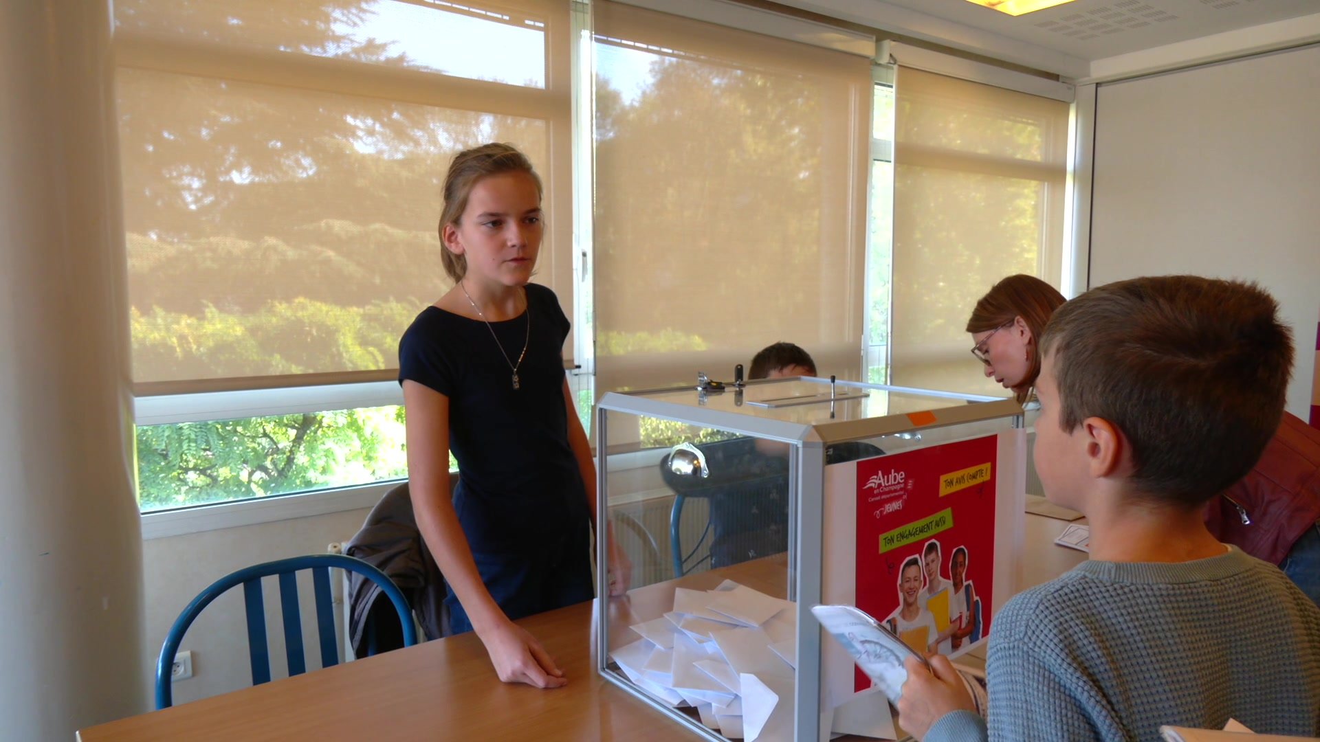Groupe de collégiens et d'élus adultes en veste de costume réunis dans une salle de classe devant un panneau roll-up Conseil Départemental Jeunes de l'Aube