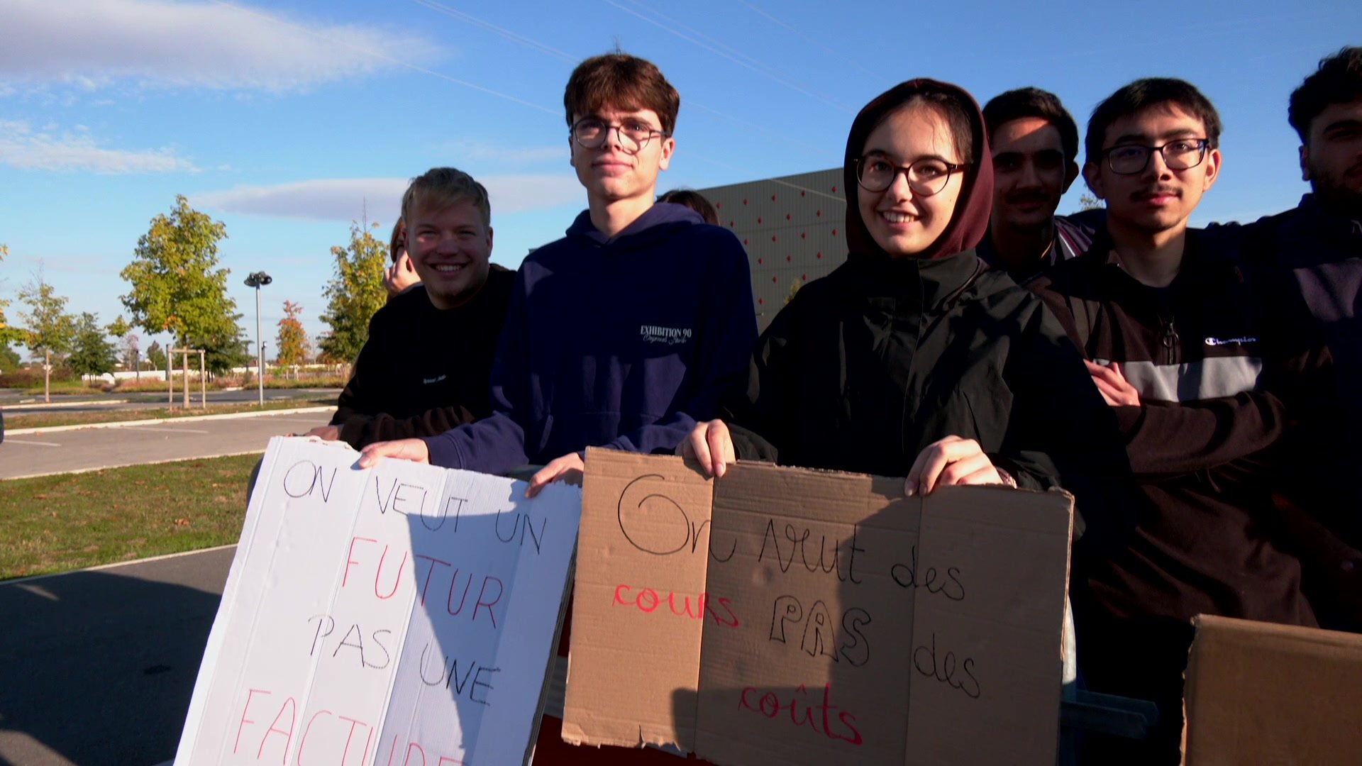 Groupe d'étudiants derrière une pancarte en carton représentant Picsou avec l'inscription L'UTT, devant un arrêt de bus indiquant Écoles d'ingénieurs, lors du blocage