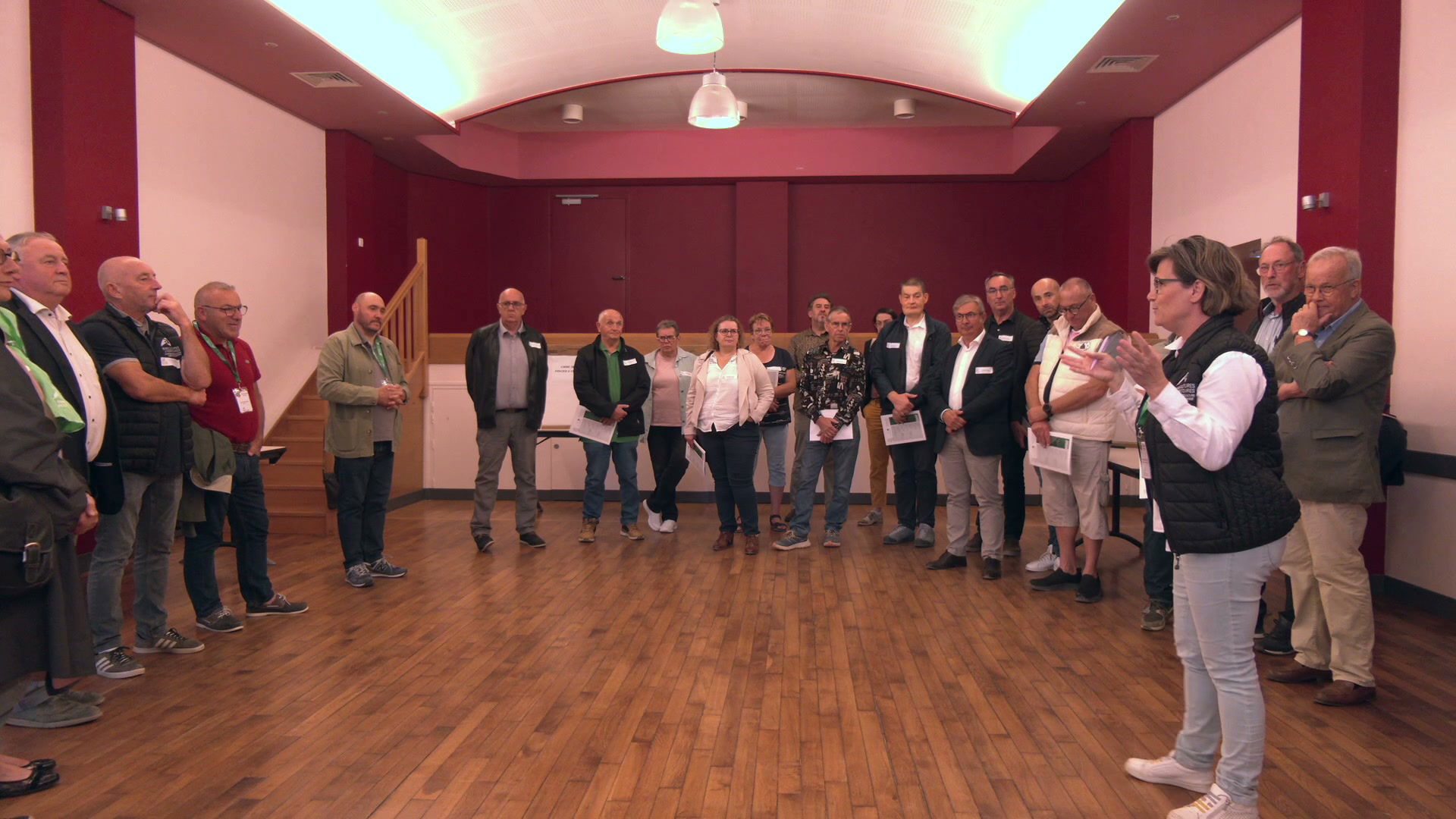 Groupe d'une vingtaine de participants debout en cercle dans une salle aux murs bordeaux lors d'une reunion agricole