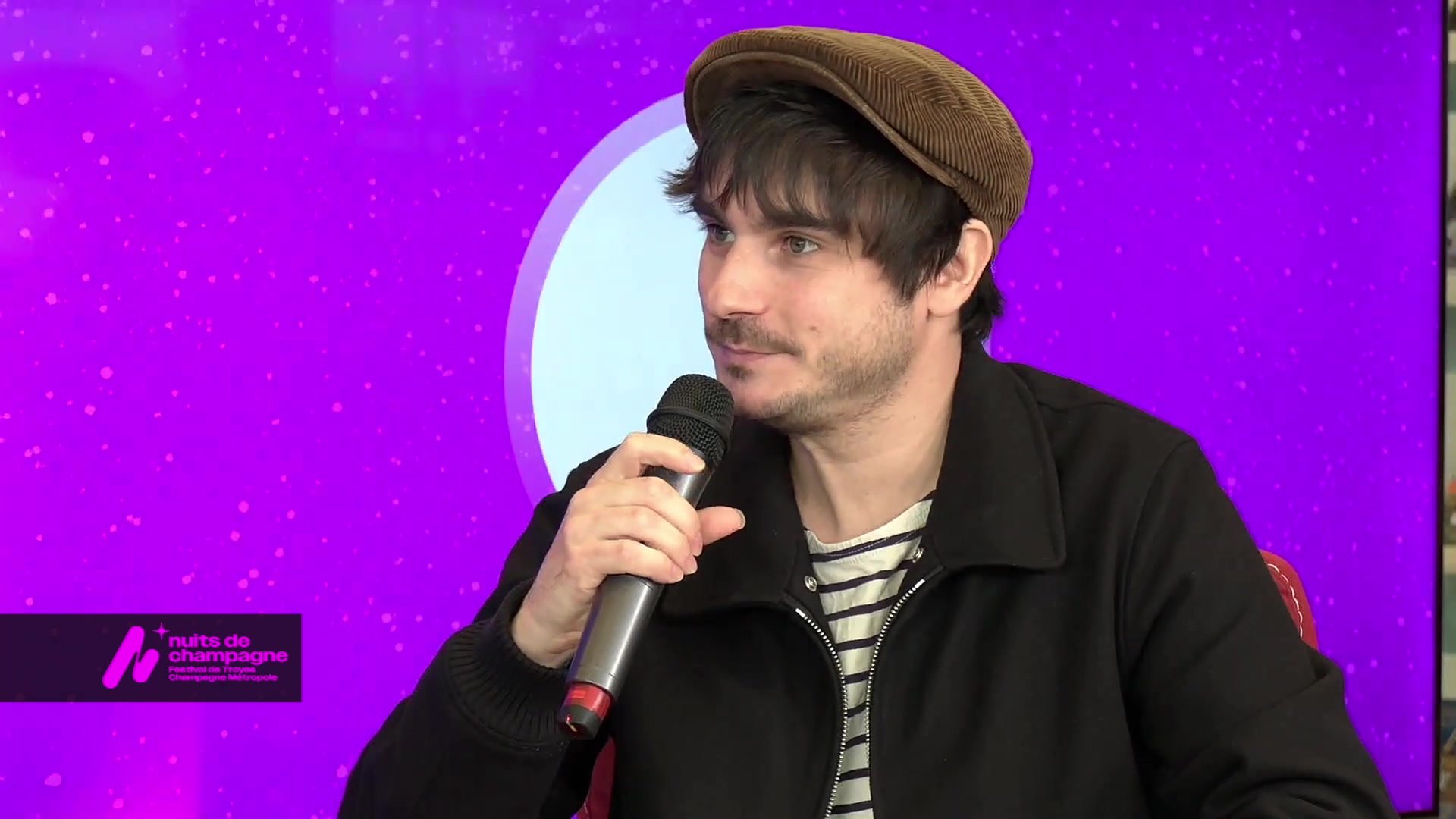 Homme au micro sur plateau violet avec logo Nuits de Champagne