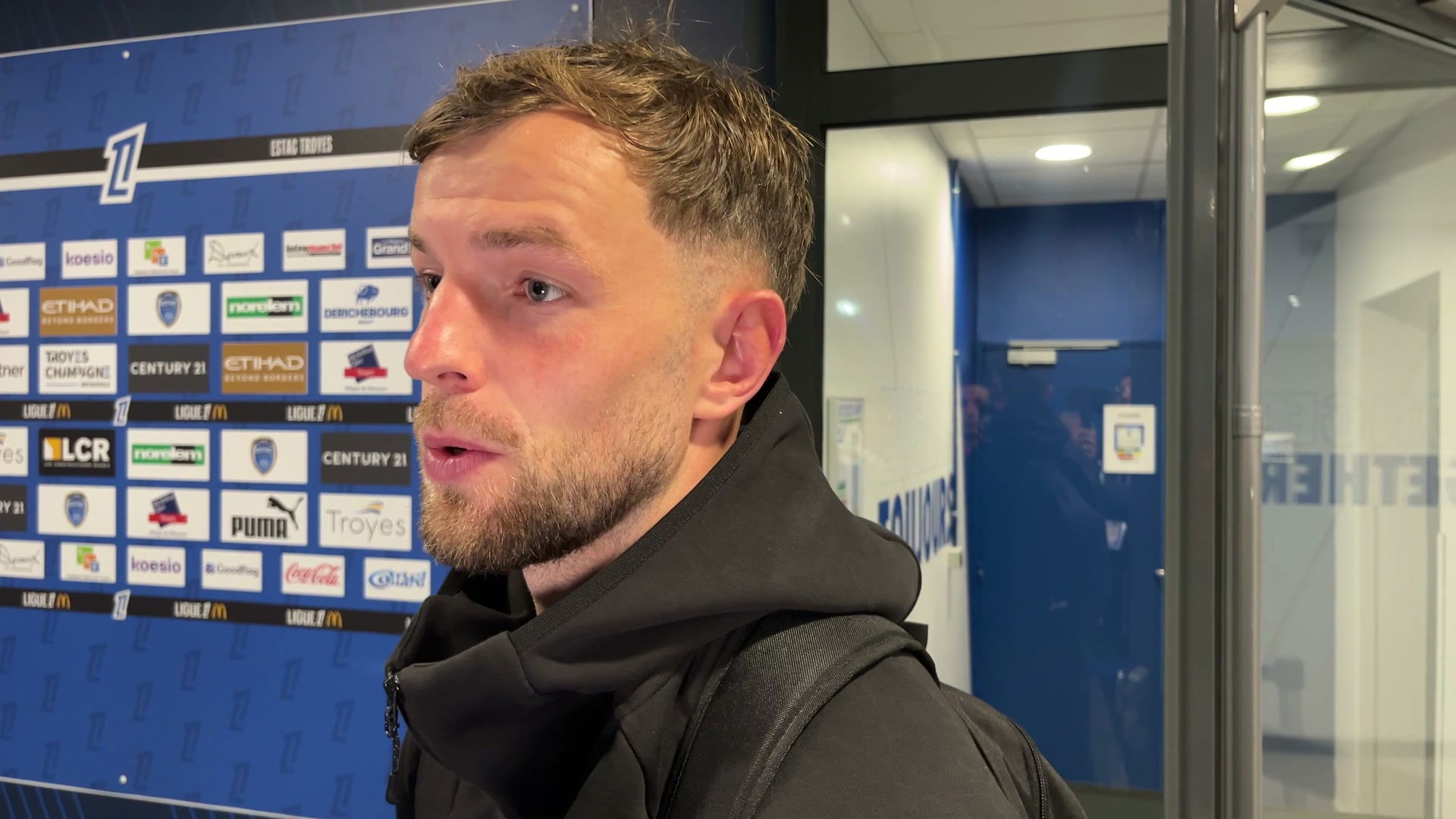 Jérémy Le Douaron en interview devant le panneau sponsors ESTAC Troyes