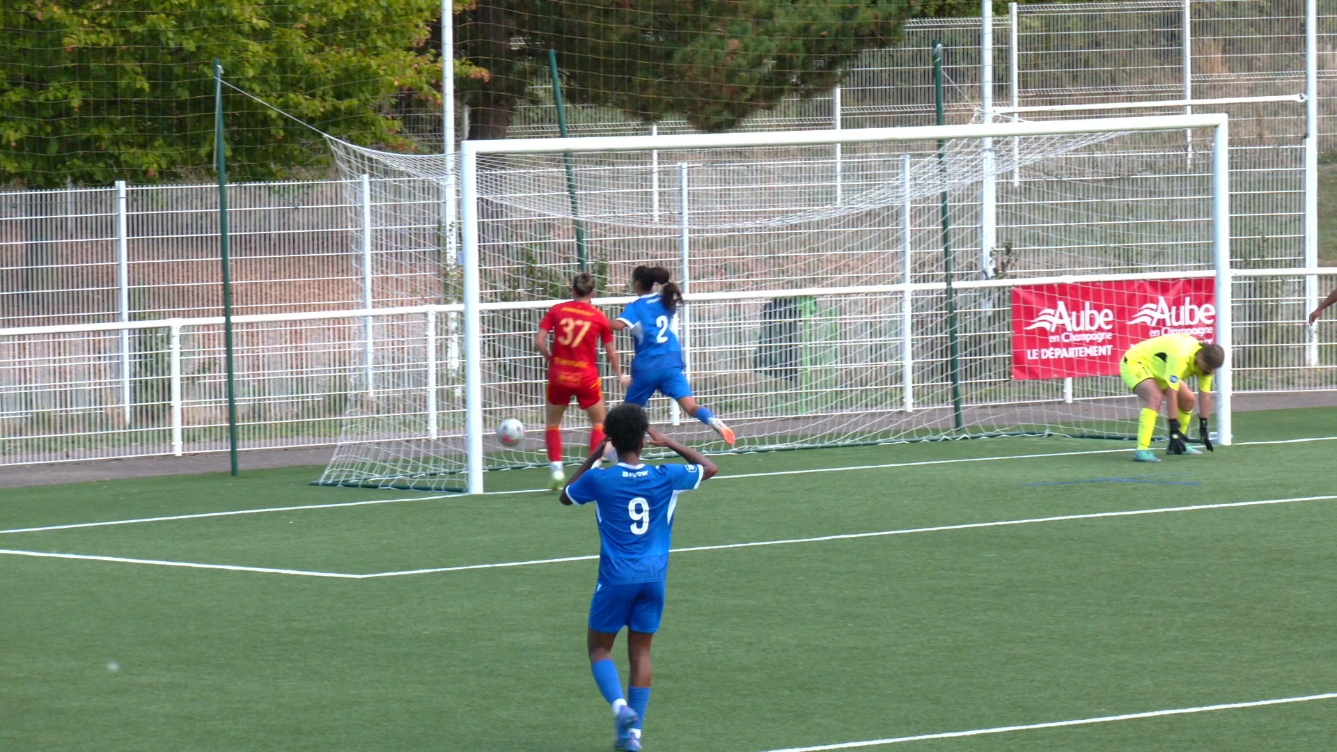 Joueuses en bleu de l'Estac devant le but adverse, gardienne en jaune penchée, panneau Aube en Champagne en fond