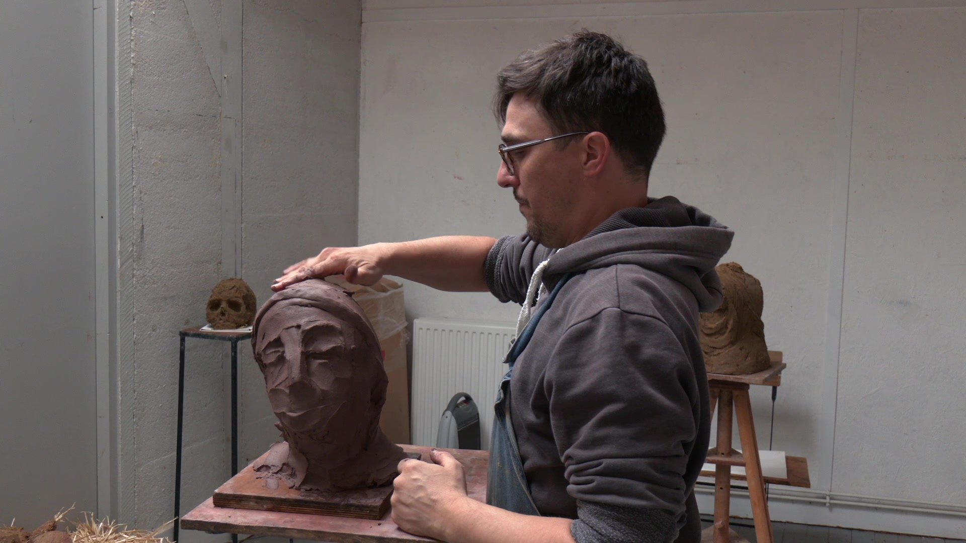 Mains d'un sculpteur modelant à mains nues une tête en argile brune, photos de sculptures classiques épinglées au mur en arrière-plan