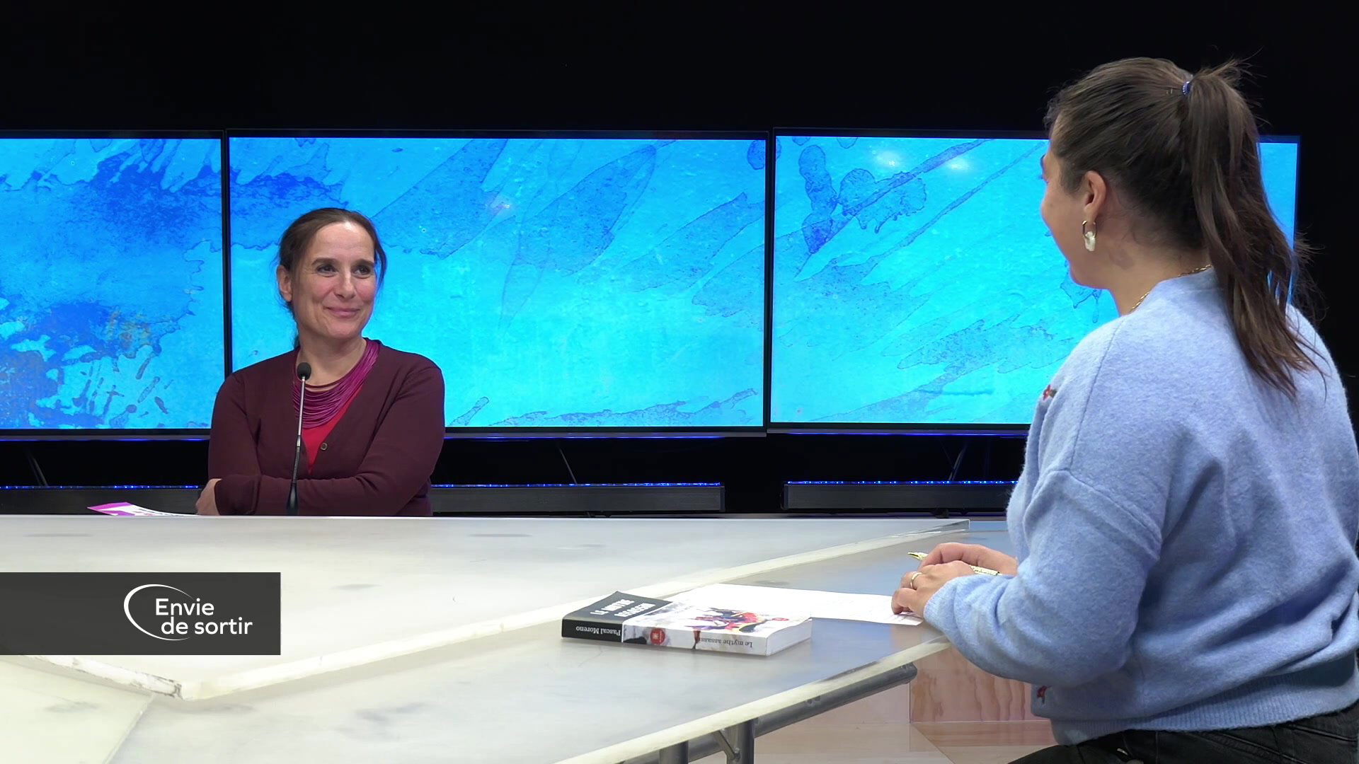 Plateau de télévision avec présentatrice et deux invités face caméra