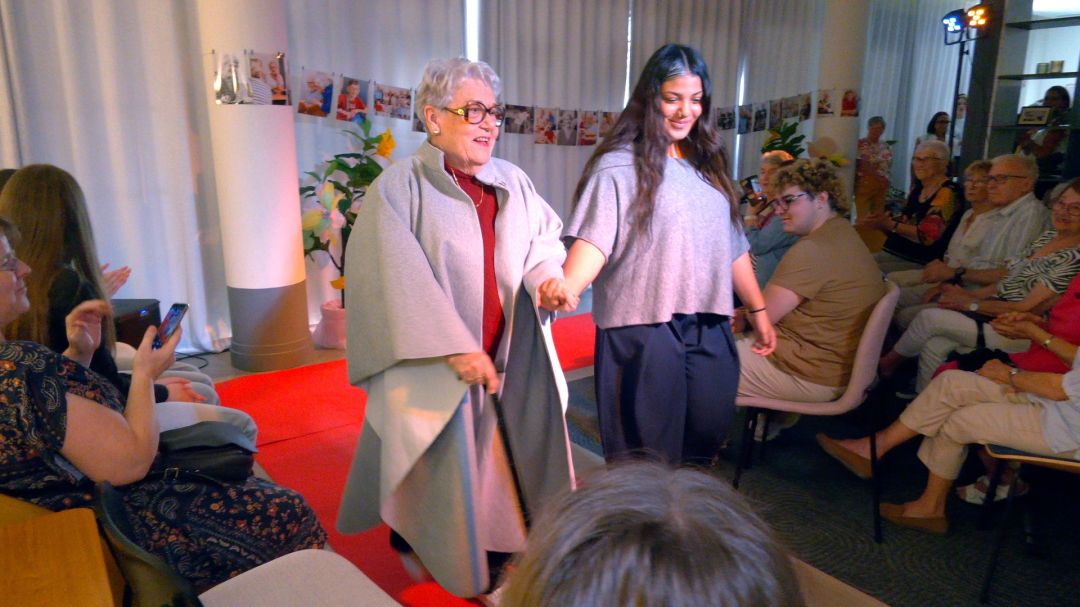 Résidente en cape grise et lycéenne main dans la main sur tapis rouge devant un public assis