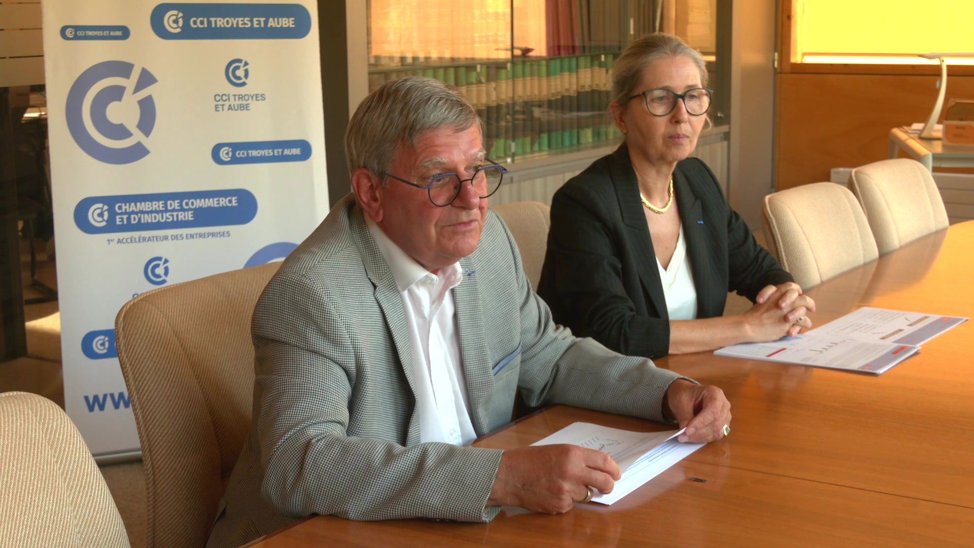 Sylvain Convers, président de la CCI Troyes et Aube, assis devant un roll-up bleu de la CCI, lunettes rondes, veste grise