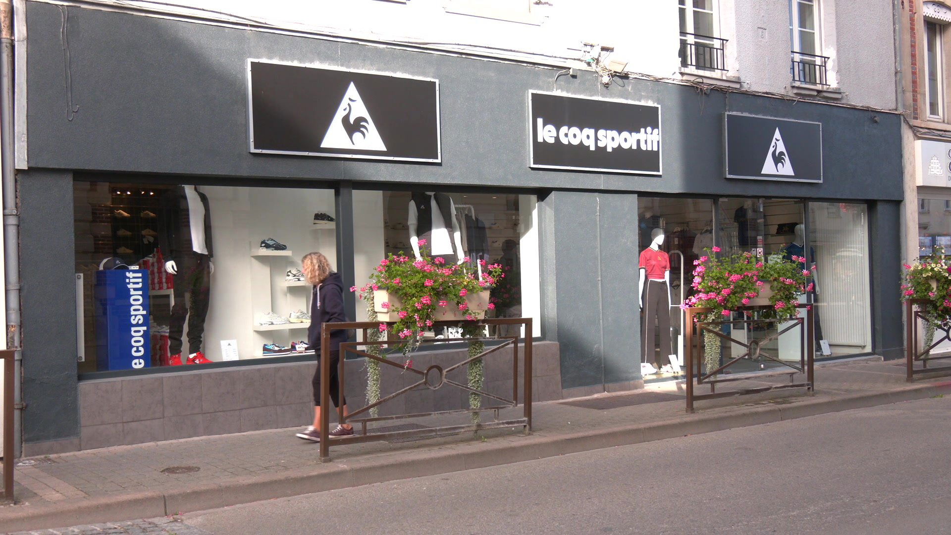 T-shirts et sweat-shirts Le Coq Sportif pliés sur des tables blanches dans la boutique de Romilly-sur-Seine, chaussures exposées sur étagères murales en arrière-plan
