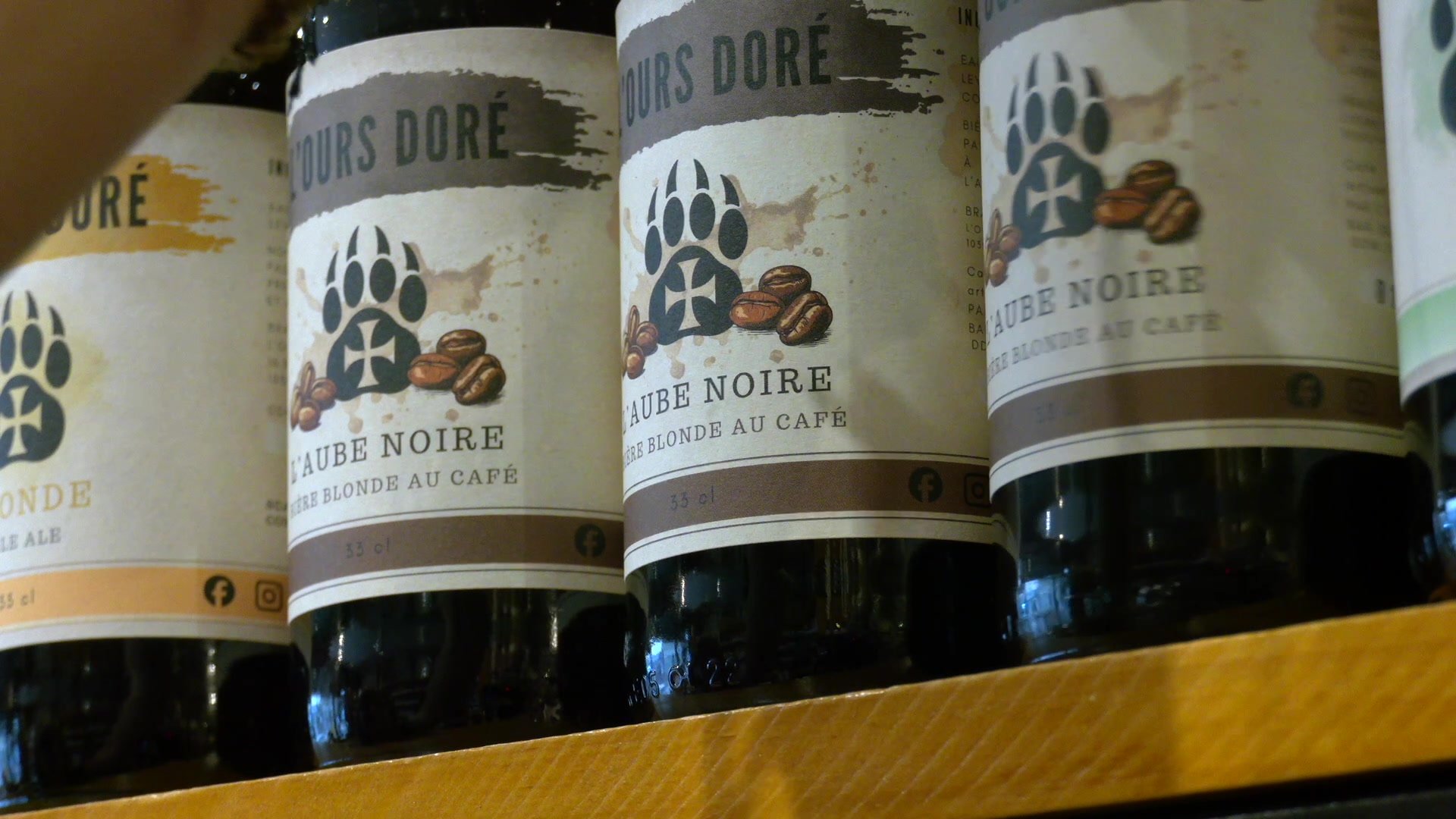 Verre estampillé L'Ours Doré tenu à la main, rempli d'une bière blonde dorée légèrement cuivrée avec une mousse blanche